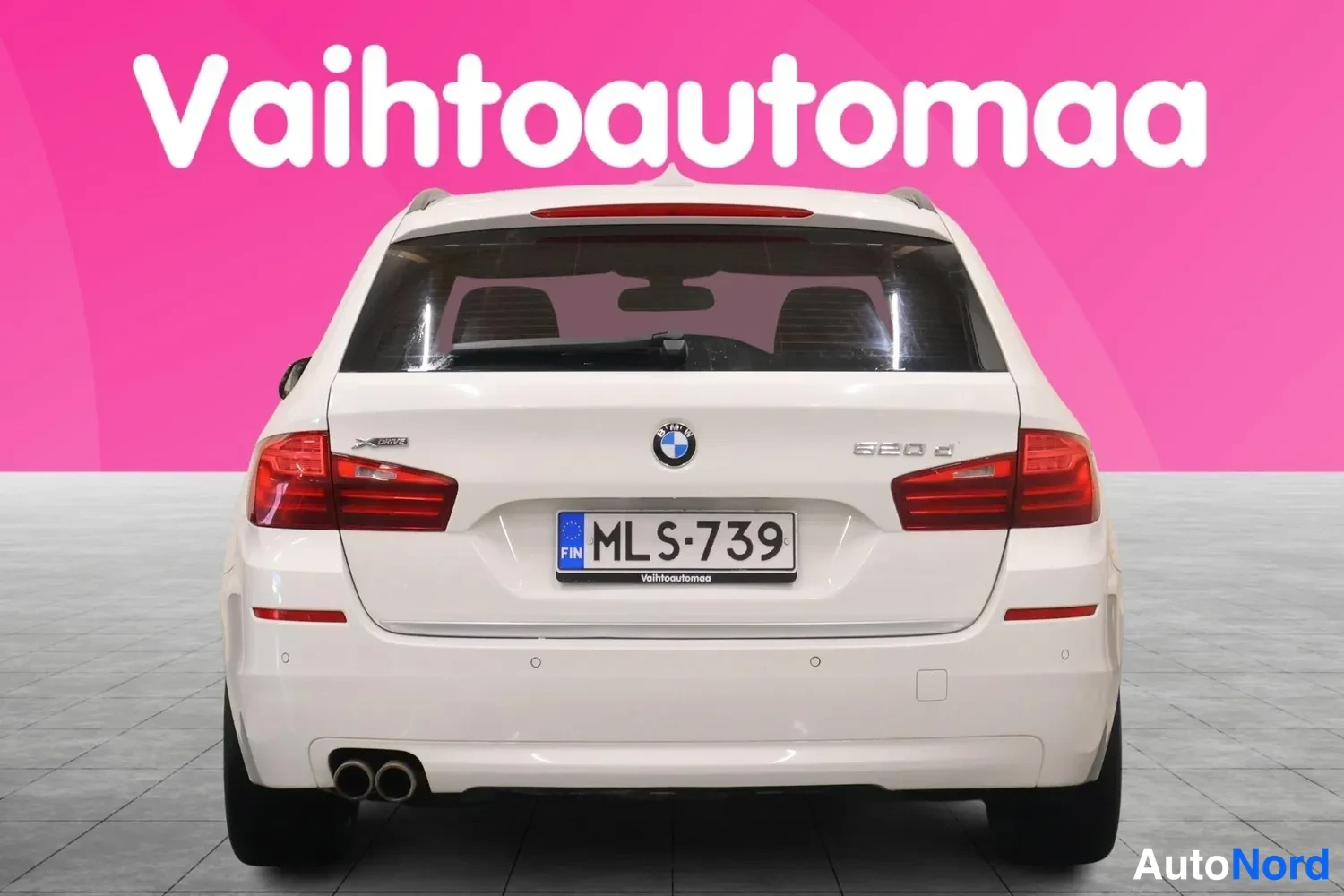 Takaa: Valkoinen farmariauto suoraan takaa, takavalo, BMW-merkki ja 520d-teksti, rekisteritunnus.