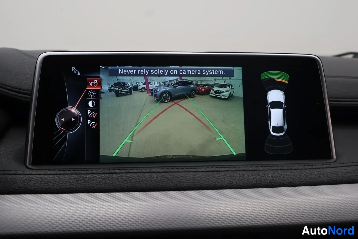Muu: Kojelaudan näyttö, jossa peruutuskameran kuva parkkihuejennelmanualilla ja tekstillä 'Never rely solely on camera system.'