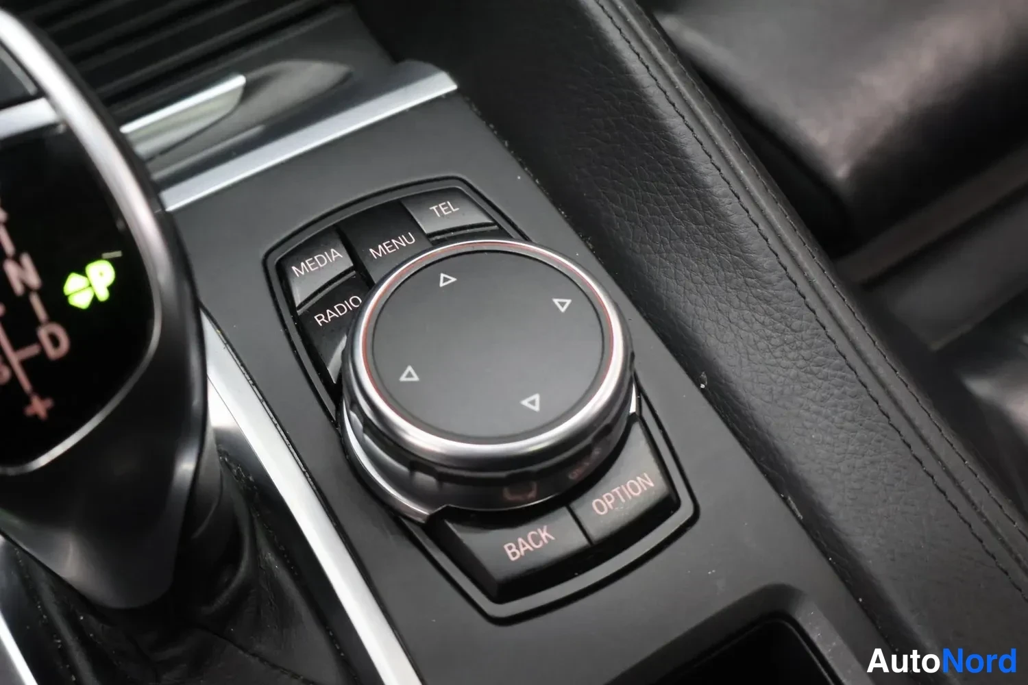Muu: BMW:n iDrive-ohjainpyörä keskikonsolissa, ympärillä painikkeet MEDIA, RADIO, MENU, TEL, BACK ja OPTION.
