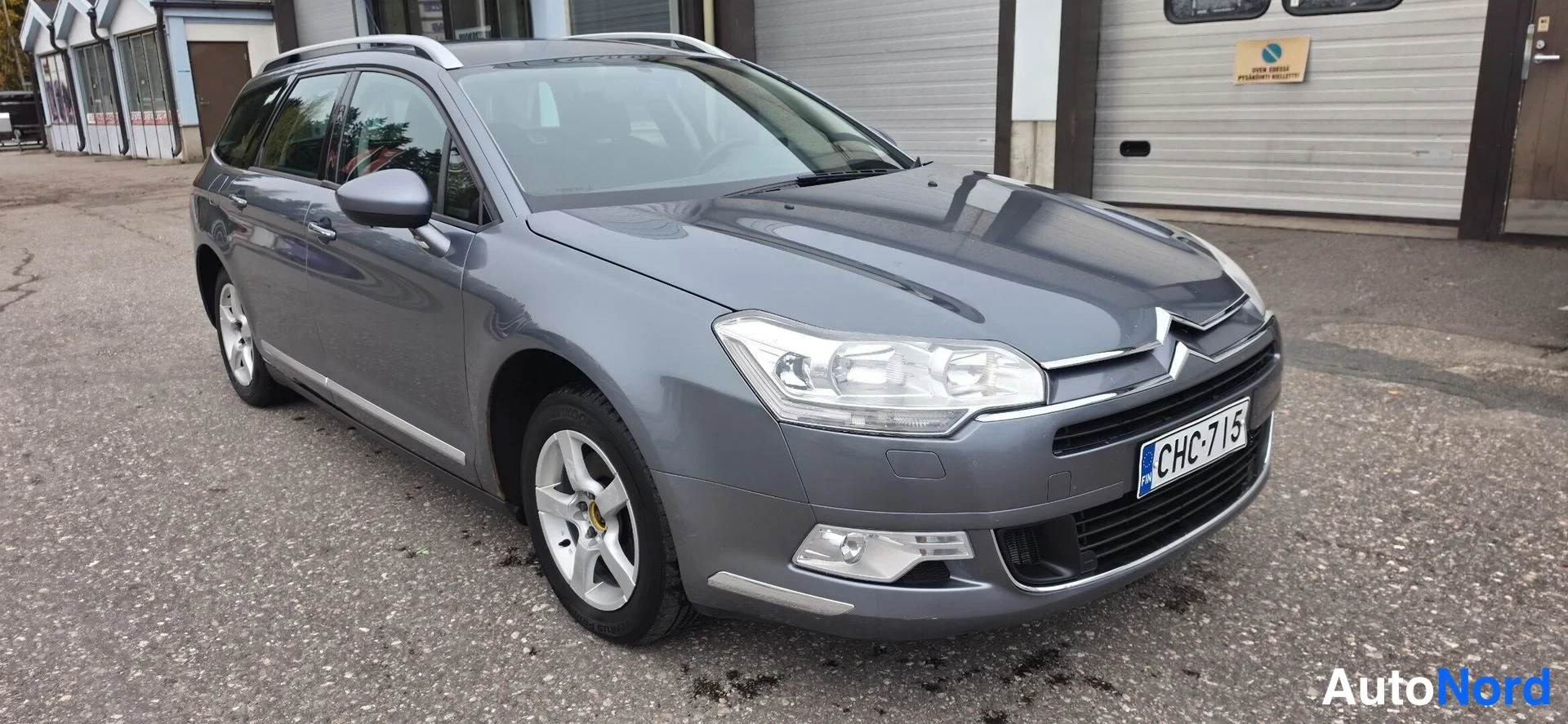 Etuviisto, nokka oikealle: Citroën C5 -farmari etuviistosta oikealta, tummanharmaa kori, rekki.