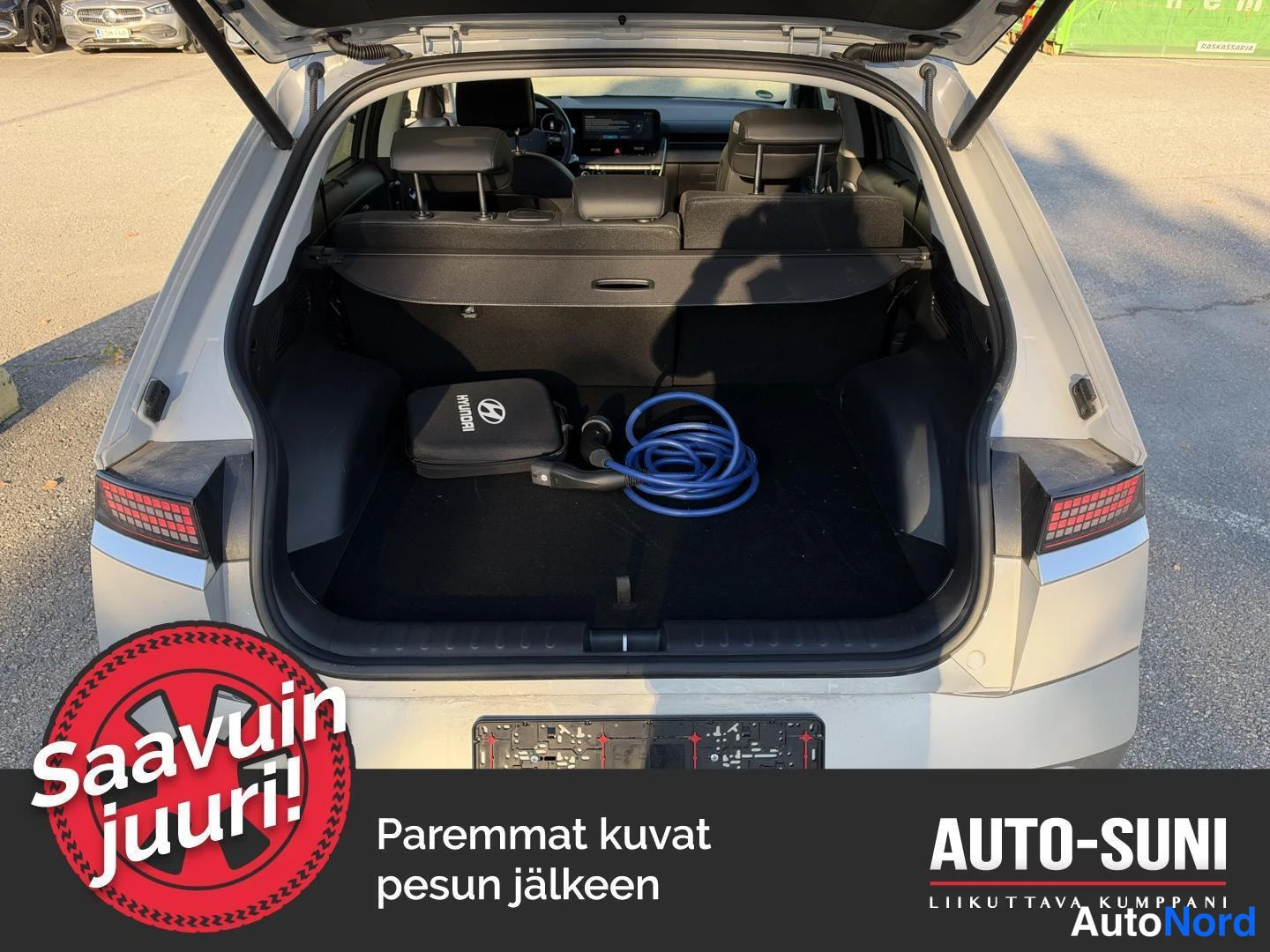 Takaa: Auton takapää auki olevine tavaratiloineen; tilissa Hyundai-laukku ja sininen latauskaapeli, punaiset takavalot näkyvissä.