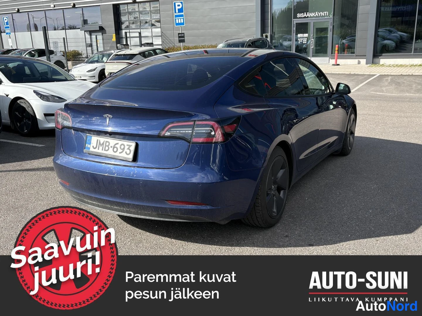 Takaviisto: Tummansininen Tesla Model 3 takaviistöstä, rekisteri, parkkialueella liikkeen edustalla.