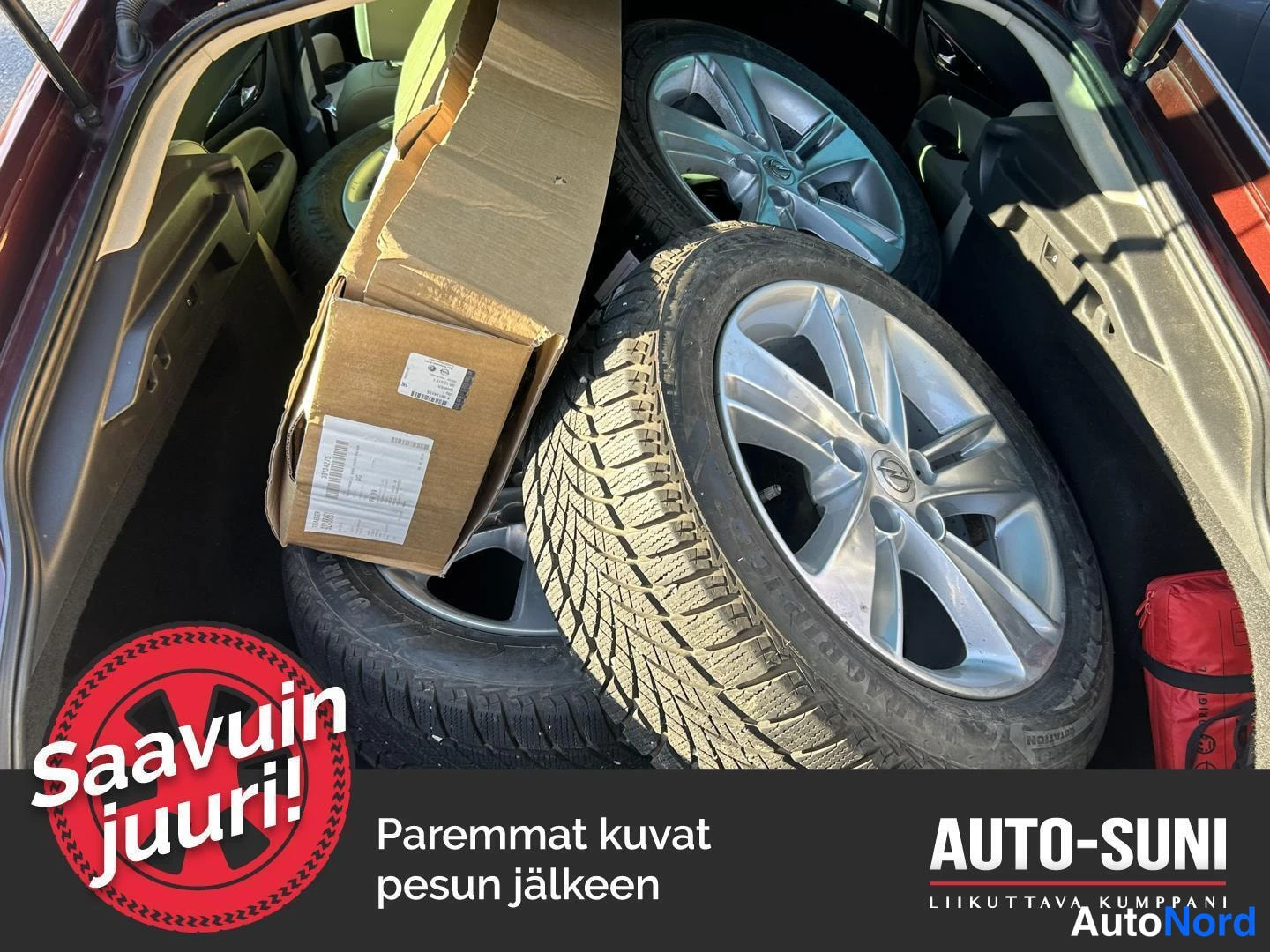 Muu: Tavaratilan sisäkuva: neljä talvirengasta Opel-merkkisillä alumiinivanteilla säilytetään laatikon ja mustan maton päällä. Punainen varuste (liuska tai kyltit) n