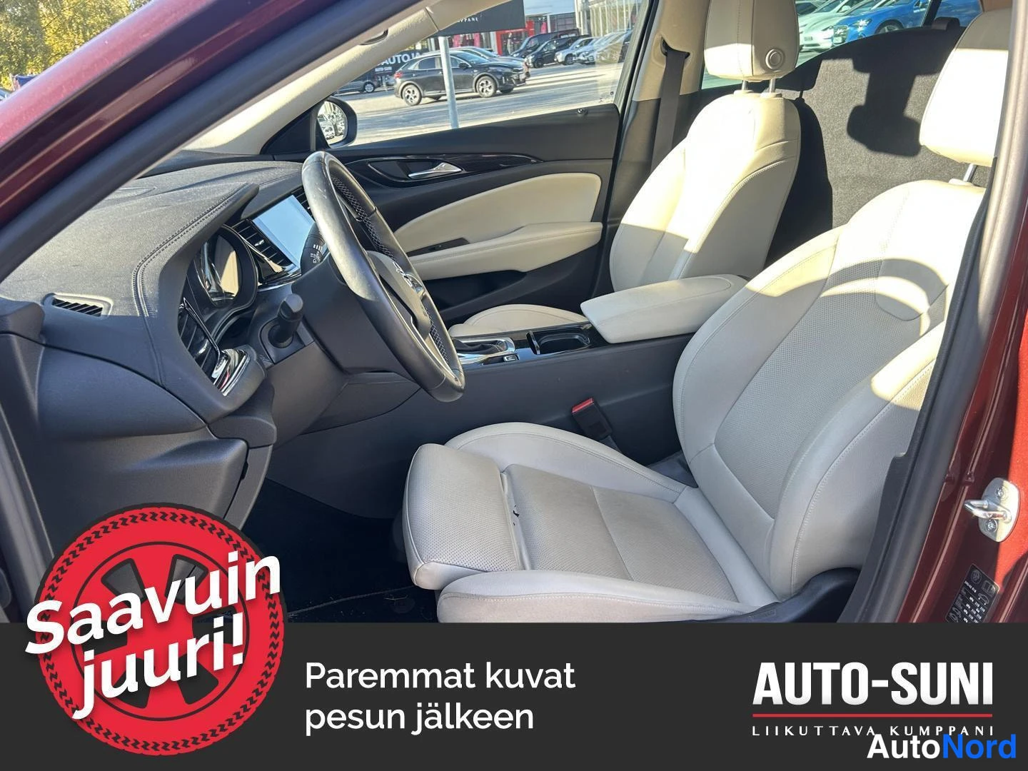 Muu: Ohjaamo sisäpuolelta: beiget nahkaistuimet, ohjauspyörä ja kojelauta; ulkona parkkipaikalla muita autoja.