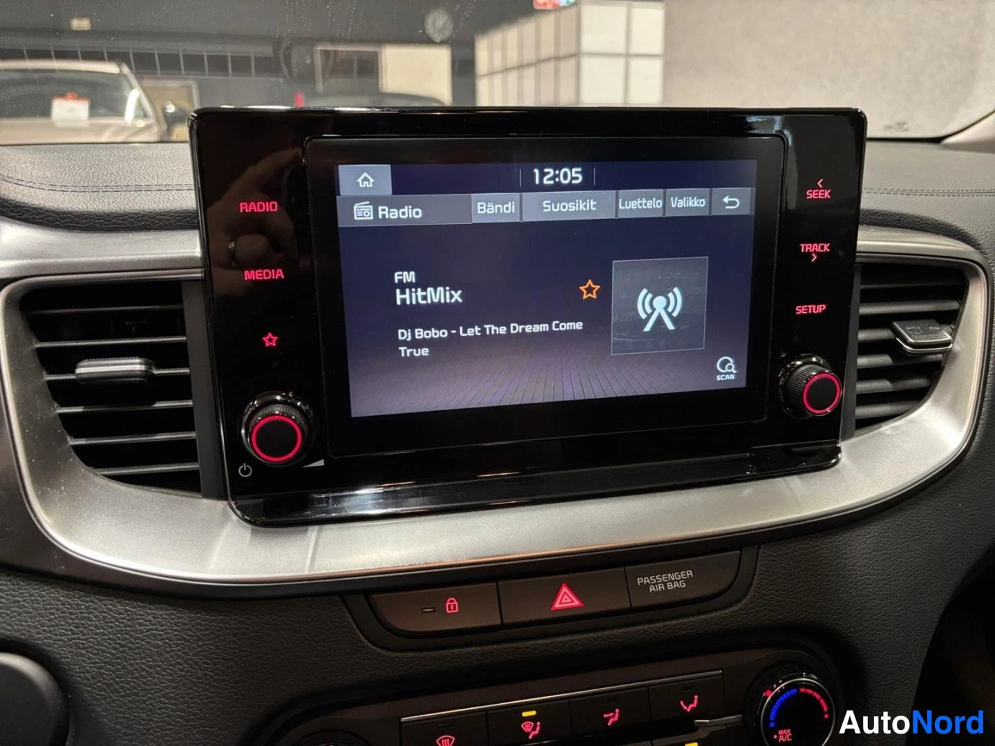 Muu: Infotainment-näytön lähikuva: radio käynnissä FM-kanavalla HitMix, kappale 'DJ Bobo - Let The Dream Come True', aikana 12:05; alapuolella PASSENGER AIR OFF -kyt