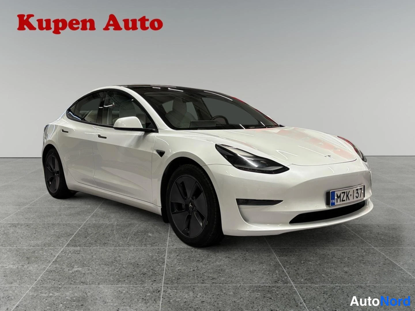 Etuviisto, nokka oikealle: Valkoinen Tesla Model 3 -sedan etukulmasta oikealta, rekisterikilpi.