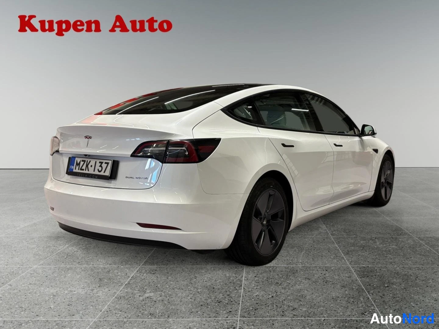 Takaviisto: Valkoisen Tesla Model 3 -sedanin takakulma vasemmalta, rekisterikilpi.