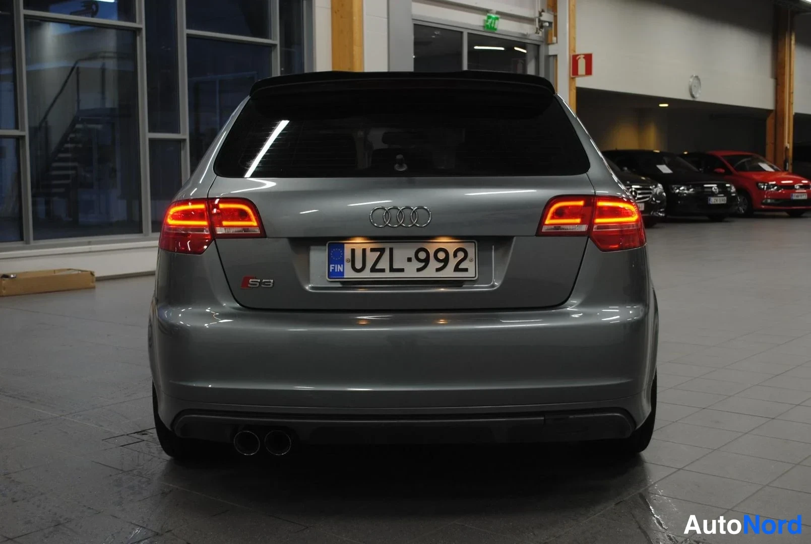 Takaa: Hopeanharmaa Audi S3 Sportback suoraan takaa kuvattuna, takavalot palavat ja rekisteritunnus on.