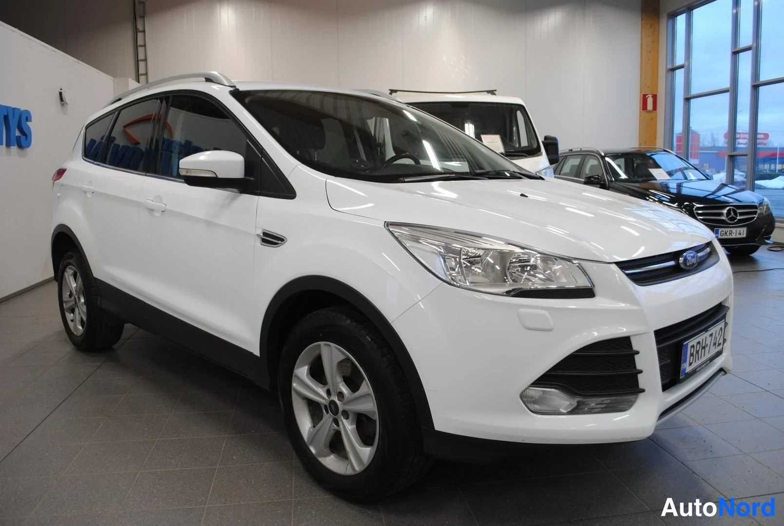 Etuviisto, nokka oikealle: Valkoinen Ford Kuga -maasturi kuvattu kolmasosakulmasta edestä oikealta autonvaraajassa, etusäiliö ja kylki näkyvissä.