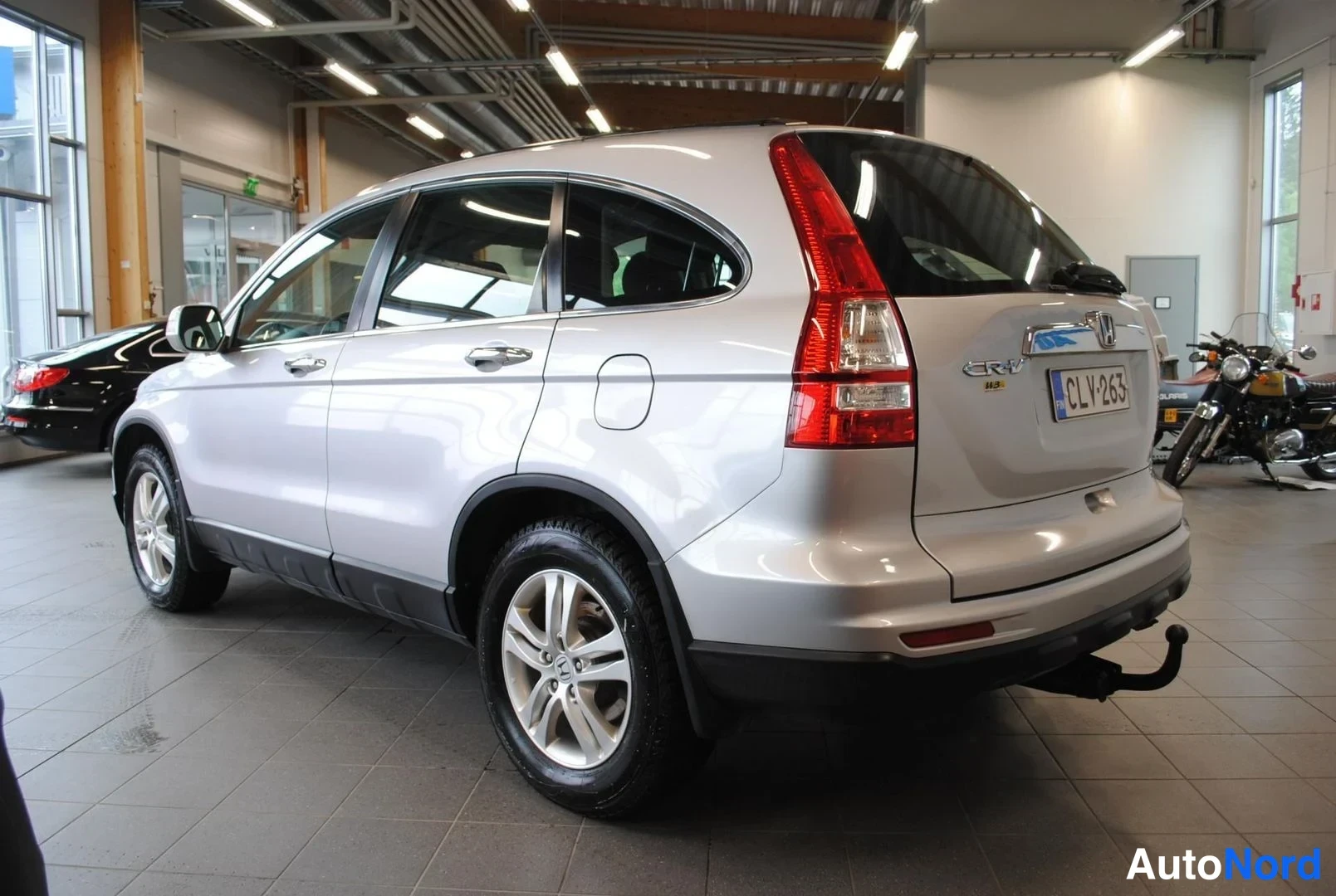 Takaviisto: Hopeanvärinen Honda CR-V takaosa ja vasen kylki näkyvissä autosalissa, CR-V-merkintä, -rekisterikilpi ja vetokoulu.