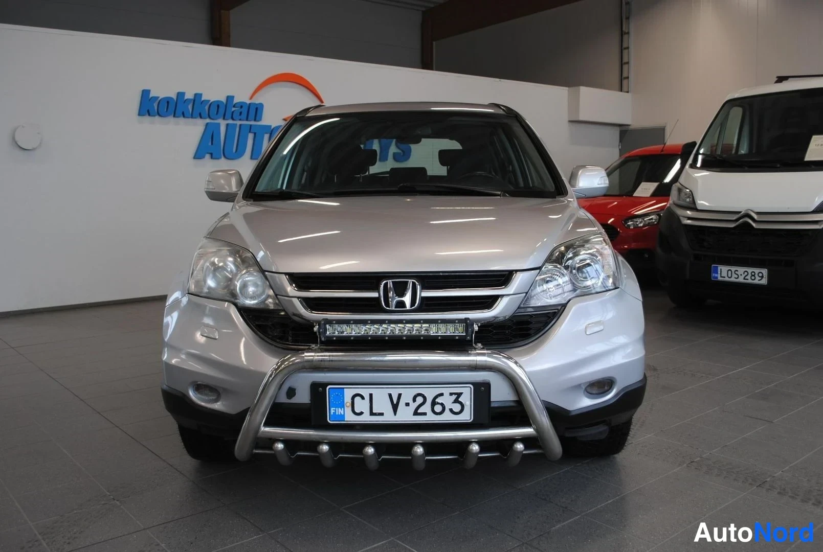 Edestä: Honda CR-V:n keulakuva suoraan edestä autosalissa; rekisterikilpi lukee ja keulassa on metallinen kaari sekä lisävalo.