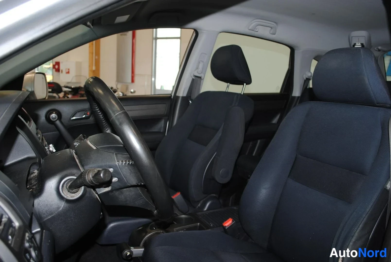 Muu: Honda CR-V:n etumatkustamon sisäkuva: tummansiniset kangasistuimet, ohjauspyörä ja kojelauta näkyvät ovista kuvattuna.