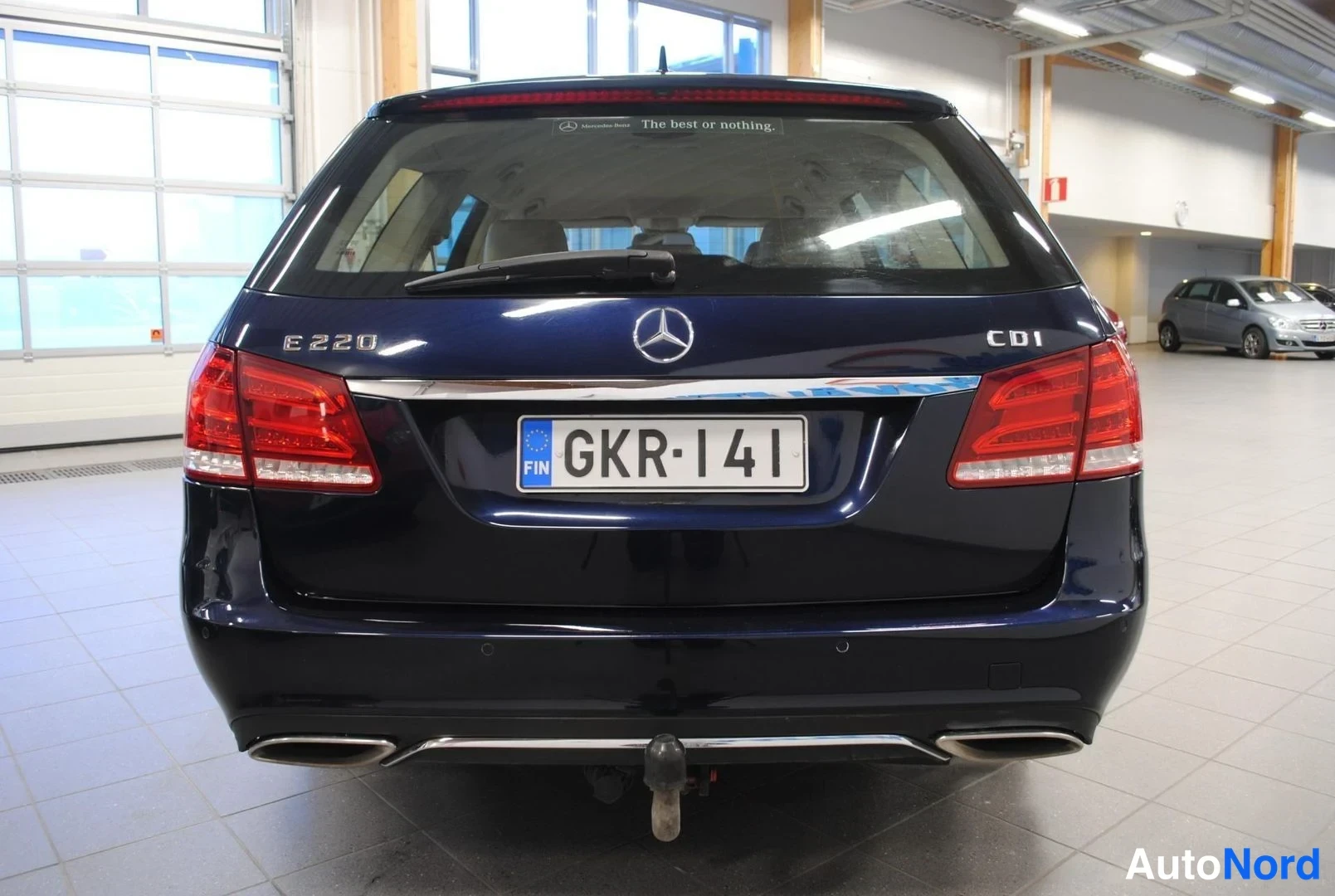 Takaa: Tummansininen farmarimerkkiauto suoraan takaa, E 220 CDI -merkinnät, rekisterikilpi ja perävaunukoukku näkyvissä.