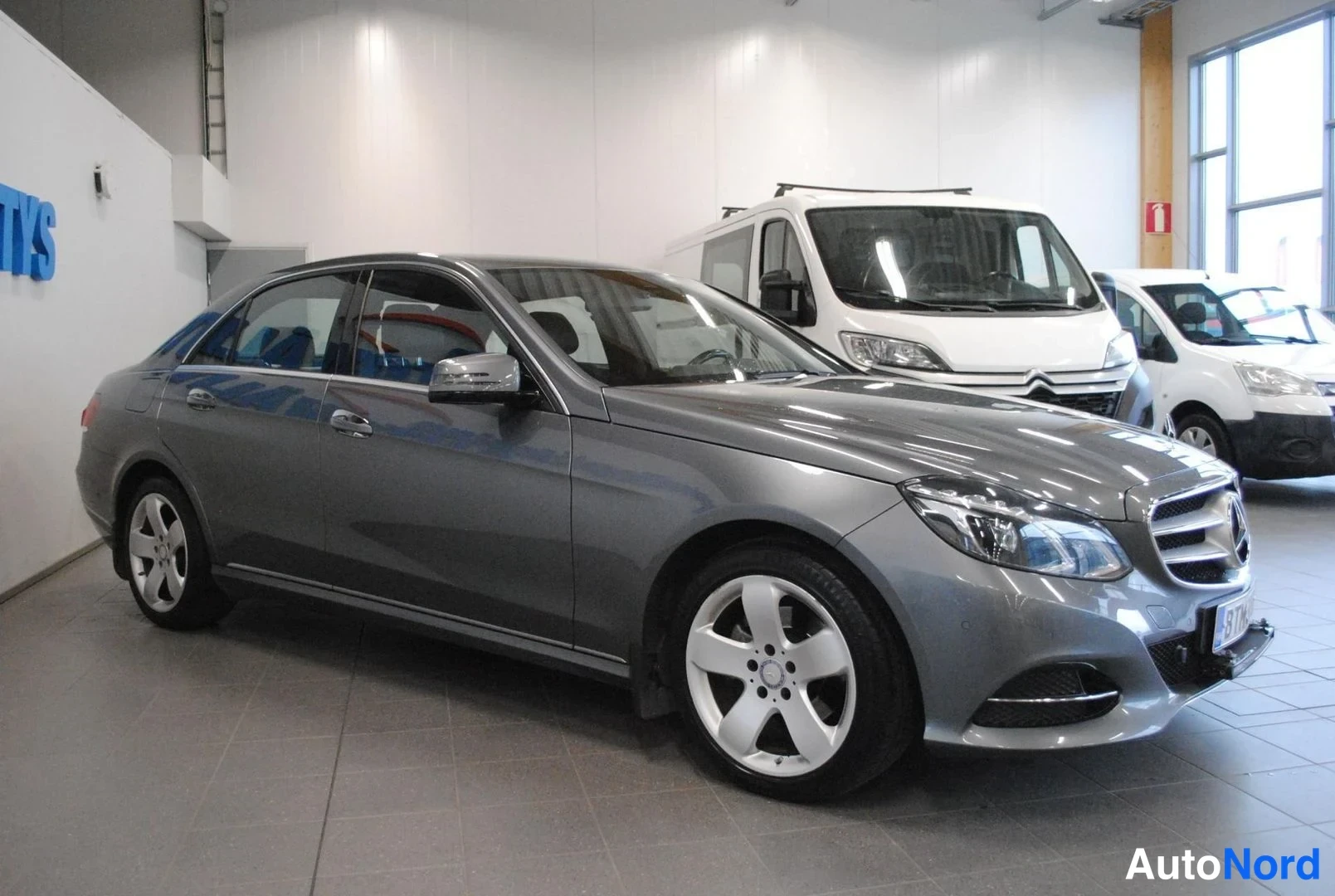 Etuviisto, nokka oikealle: Mercedes-Benz E-sarjan sedan sivuviistosta oikealta, tummanharmaa kori ja Hopeanvalkoiset peltivanteet