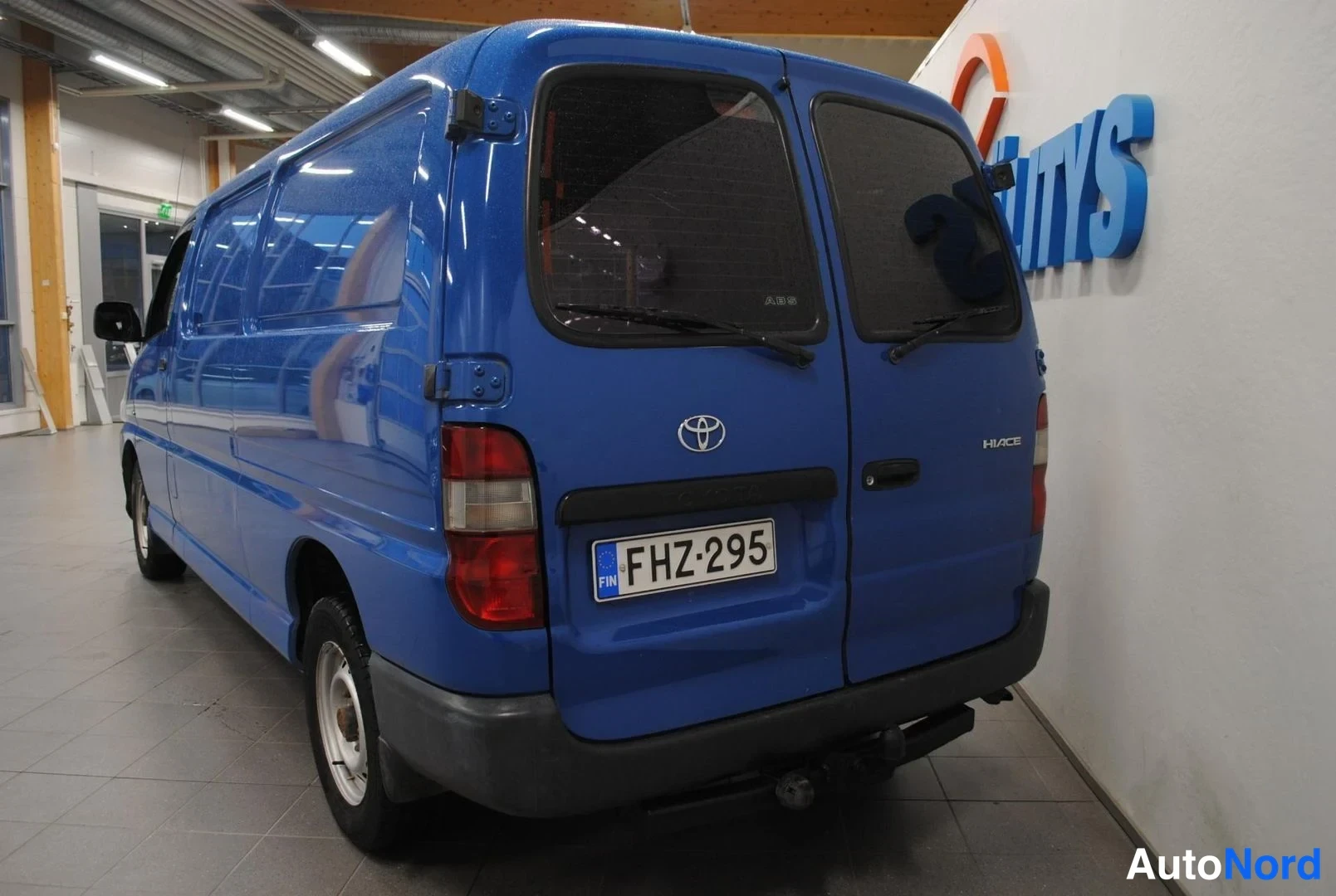 Takaviisto: Sininen pakettiauto takaa vasemmalta, peräluukulla Toyota-merkki ja teksti HIACE, rekisterikilpi.