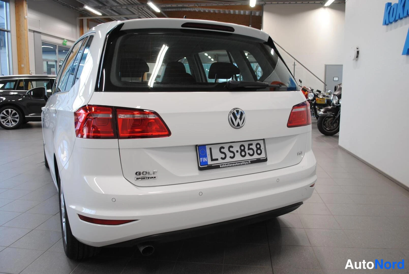 Takaa: Valkoinen Volkswagen Golf Sportsvan takaa kuvattuna; näkyvissä Volkswagen-merkki, punaiset takavalot, TSI-merkintä, rekisterikilpi ja Golf Sportsvan -teksti.