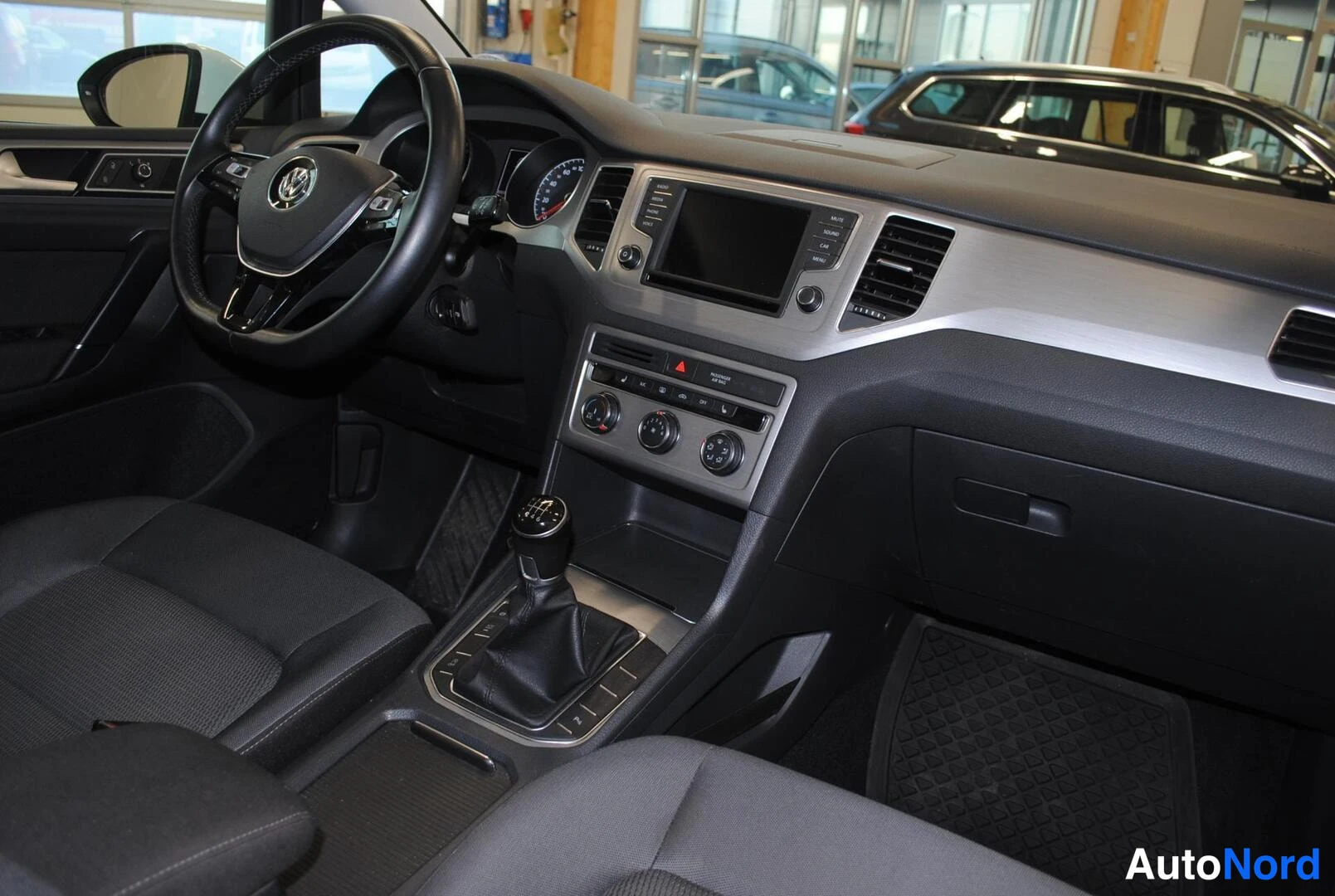 Muu: Ohjaamosta kuvattu näkymä: Volkswagen-ohjauspyörä, mittaristo, keskinäyttö, radionäppäimet, ilmastointinupit ja manuaalivaihtoaike.