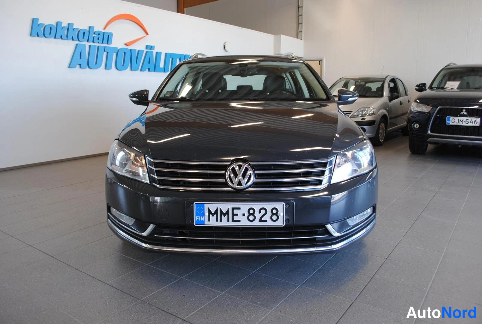 Edestä: Tumman auton etunäkymä suoraan edestä, Volkswagen-merkki ja rekisterikilpi.