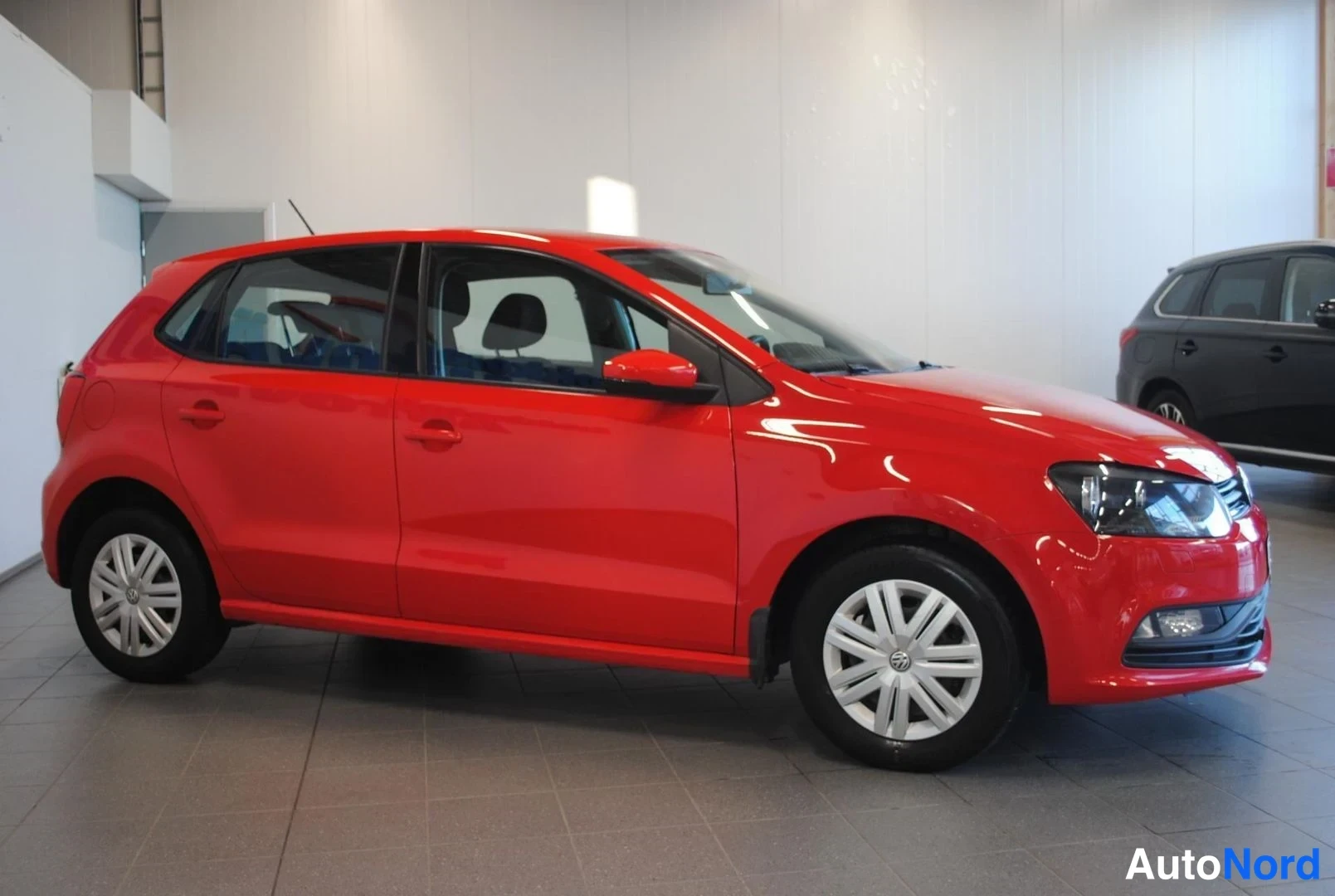 Etuviisto, nokka oikealle: Punainen Volkswagen Polo sivulta etukulmasta, oikea kylki ja keula näkyvissä.
