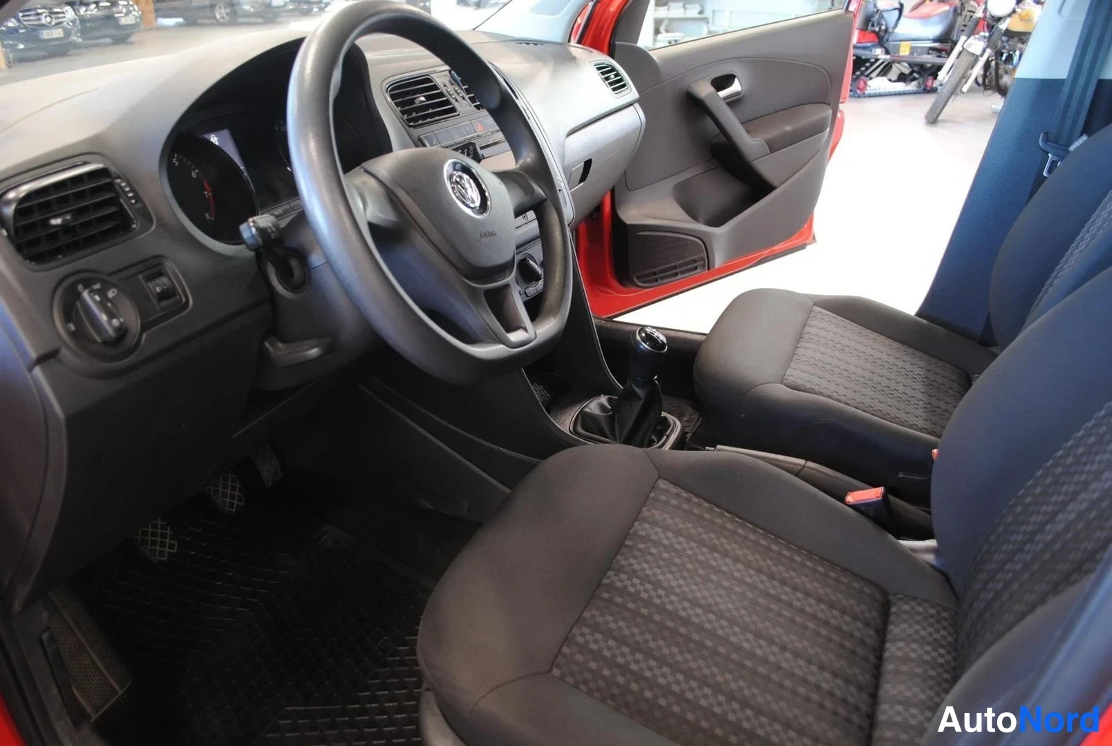 Muu: Auton sisätilat: kuljettajan puolen ohjaamo, ratissa Volkswagenin merkki, manuaalivaihteen keksi ja tummat kangasistuimet, ovi auki punaisena.
