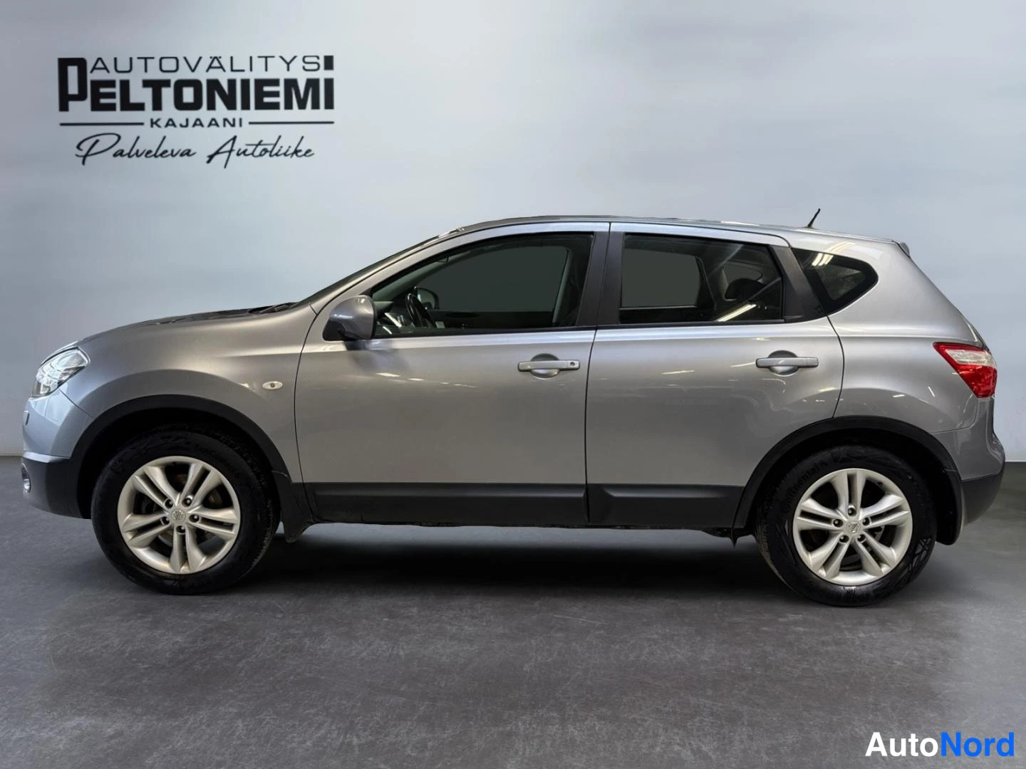 Sivulta: Hopeanharmaa Nissan Qashqai sivusta kuvattuna autosalonia valkoista taustaa vasten.