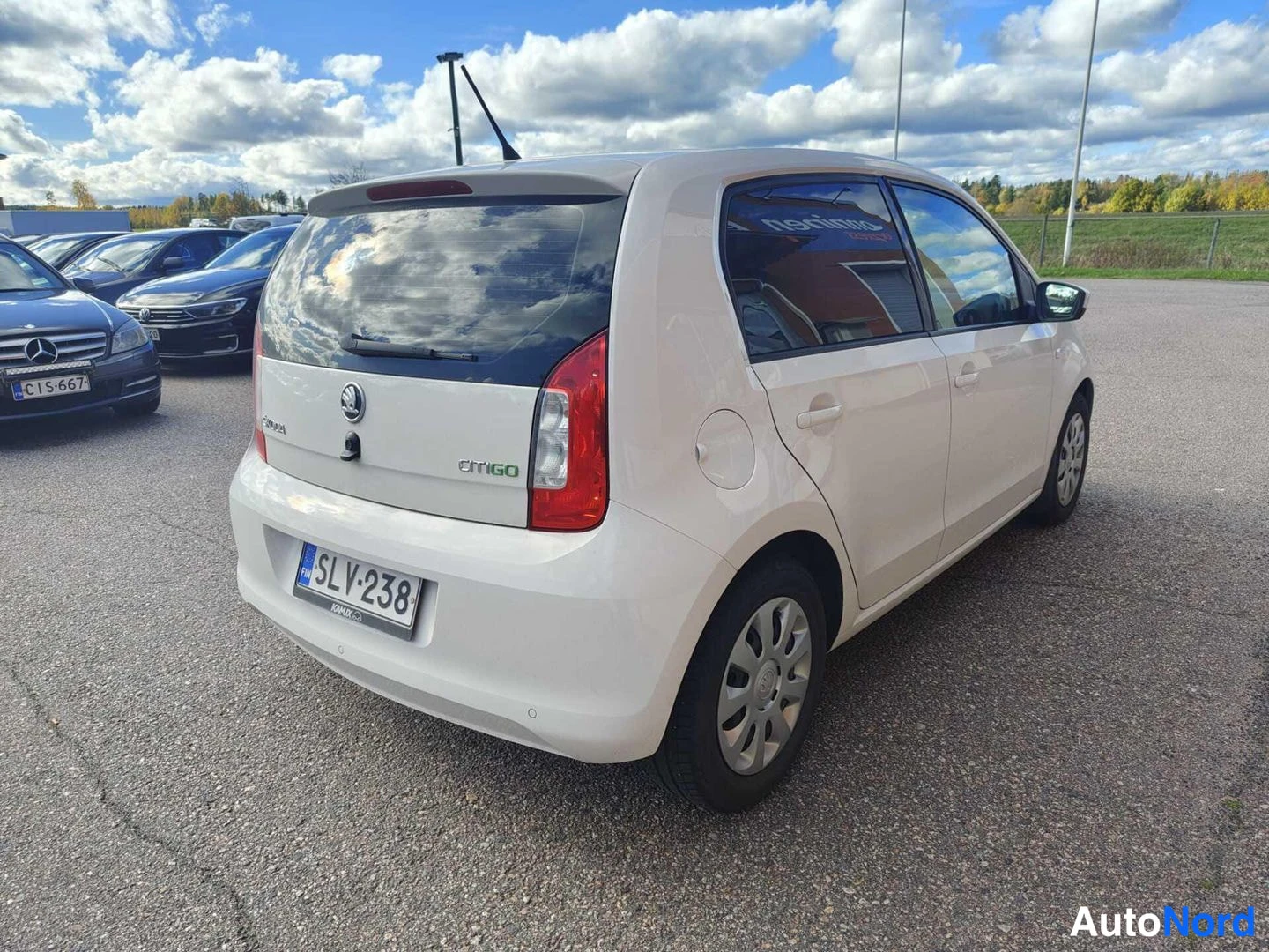 Takaviisto: Valkoinen Skoda Citigo CitiGO -merkinnällä kuvattuna takaa vasemmalta kolmivirtauksesta parkkipihalla. Takavalo, logot ja rekisterikilpi näkyvät, taustalla muit