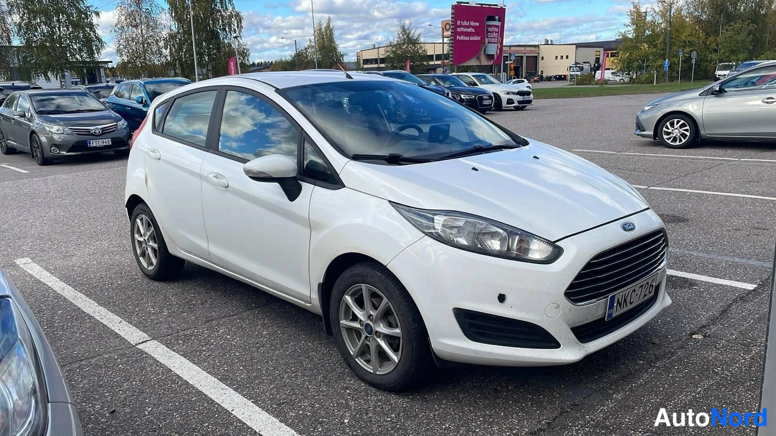 Etuviisto, nokka oikealle: Valkoinen Ford Fiesta viistosti edestä oikealta kuvattuna parkkialueella.
