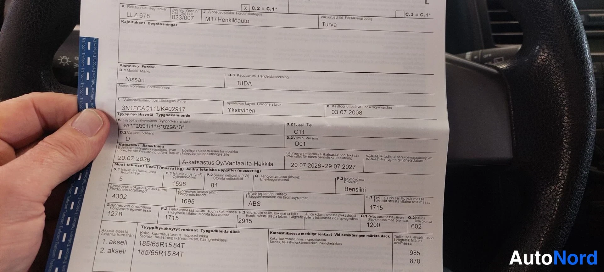 Muu: Käden pitämä ajoneuvon katsastusraportti Nissan Tiidasta, jossa näkyvät rekisteritiedot, mittarilukema 1715 ja kesä-/talvirenastiedot.