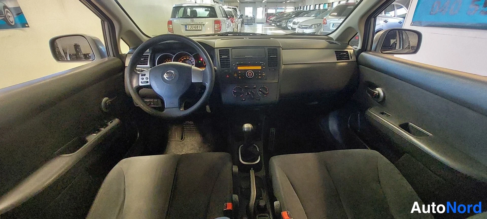 Muu: Nissan Tiidan sisätilat: ohjauspyörä, kojelauta, manuaalivaihdeila ja kaksi etuistuinta.