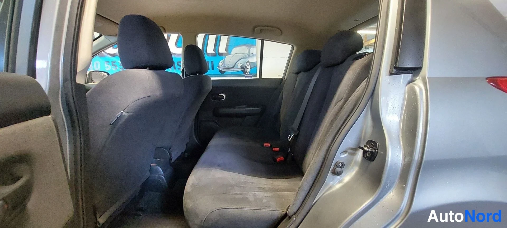 Muu: Nissan Tiidan takaistuin tummilla kangaspenkeillä, takiovi auki.