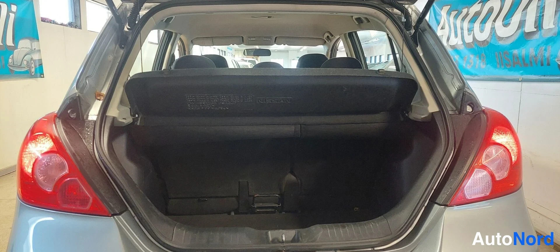 Muu: Nissan Tiidan auki avattu tavaratila, takavalojen välistä näkyvä taustapaneeli.