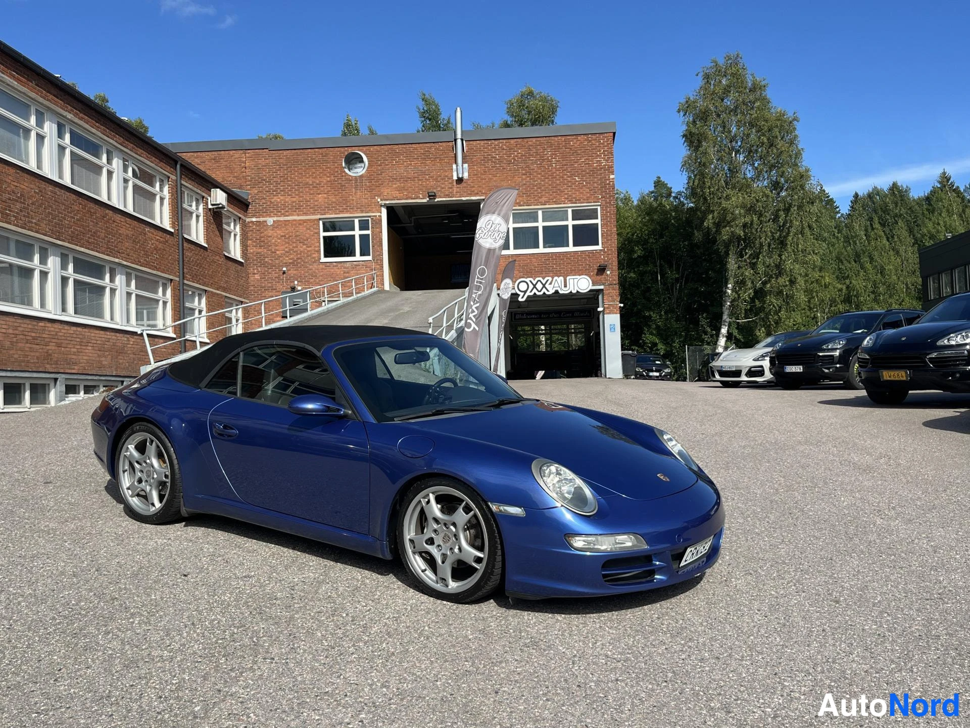 Etuviisto, nokka oikealle: Sininen Porsche 911 Cabriolet kolmivartalokuvassa nenä oikealla, musta katto, hopeiset kevytmetallivanteet.