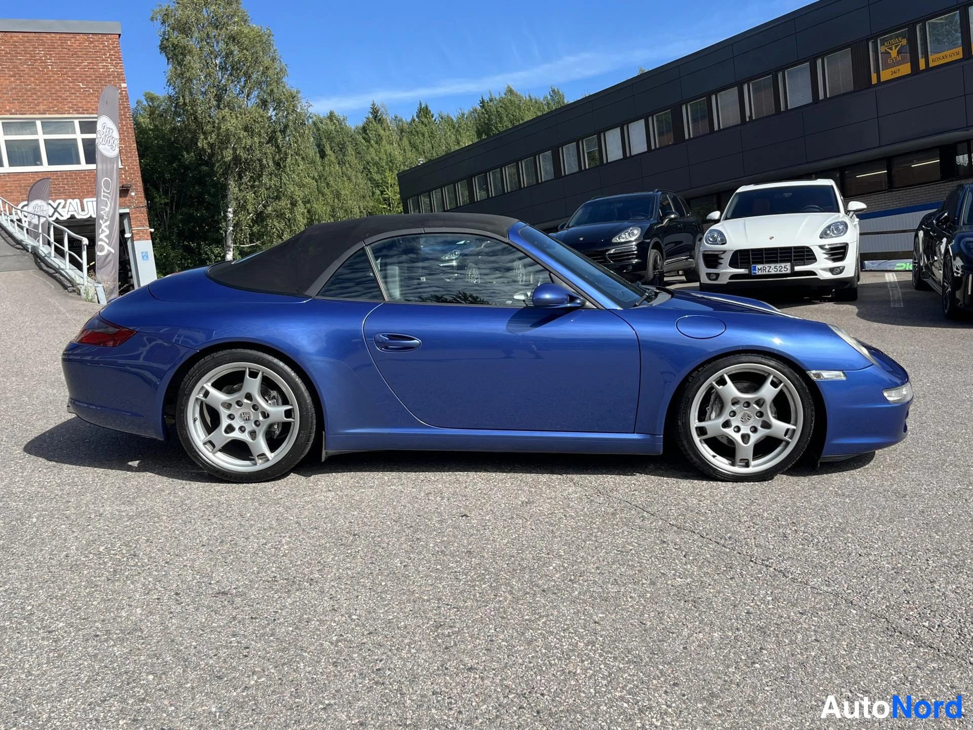 Etuviisto, nokka oikealle: Sininen Porsche 911 Cabriolet profiilikuva oikealta, musta katto, hopeiset kevytmetallivanteet.