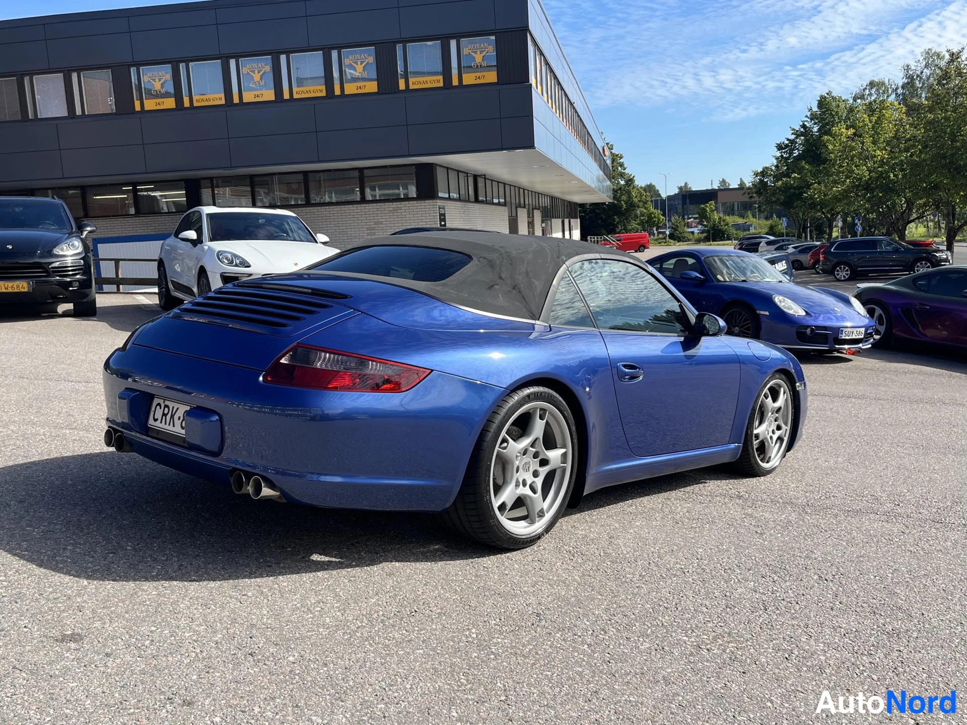 Takaviisto: Sininen Porsche 911 Cabriolet takaviistokuva, musta katto, kromiputket takapuskurissa, rekisteri.