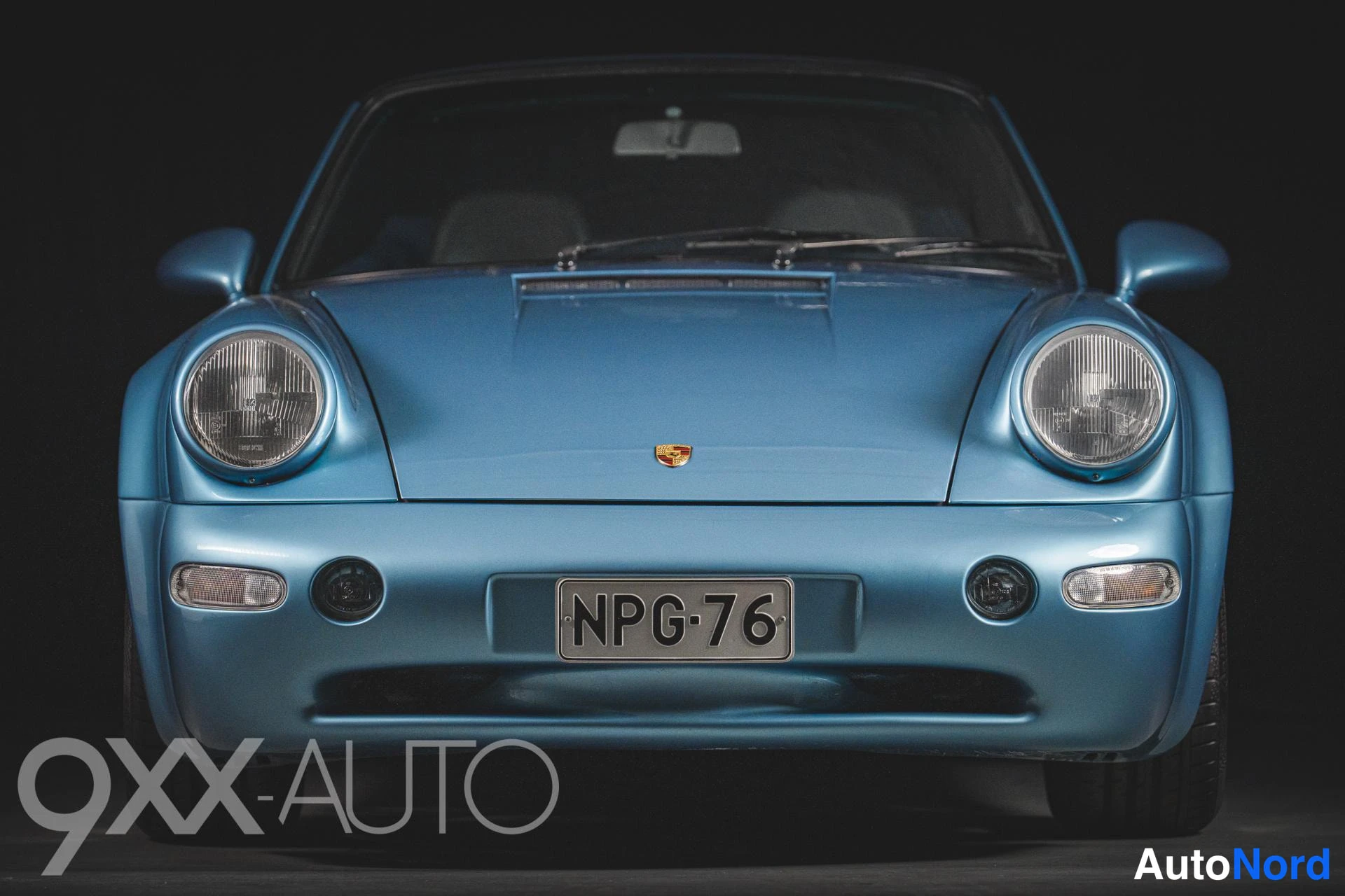 Edestä: Sininen Porsche-avomalli suoraan edestä, pyöreät ajovalot ja musta katto, rekisteritunnus.