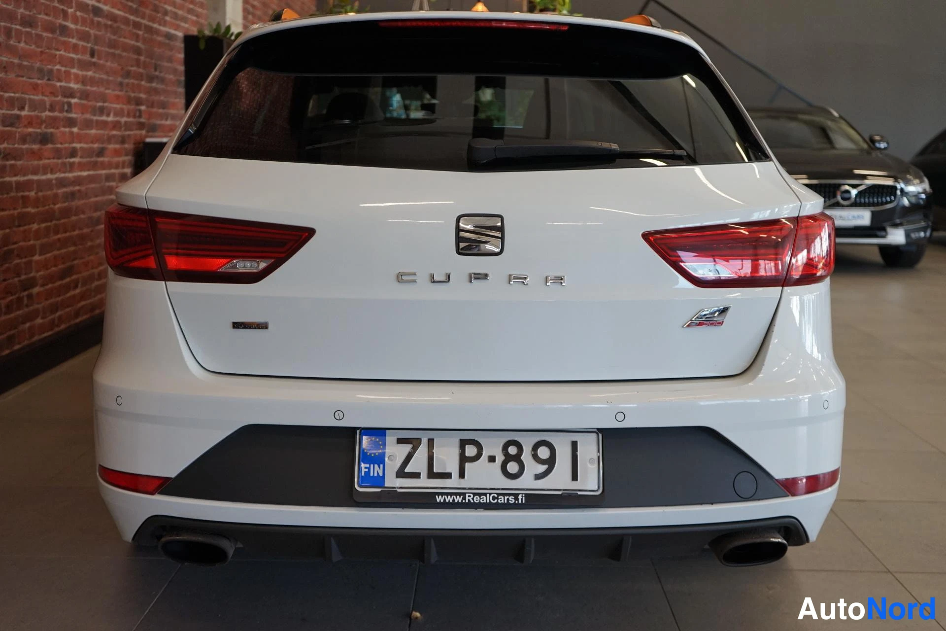 Takaa: Valkoisen auton takanäkymä: CUPRA-teksti takaluukussa, punaiset takavalot, kaksoispakoputket, rekisteritunnus.