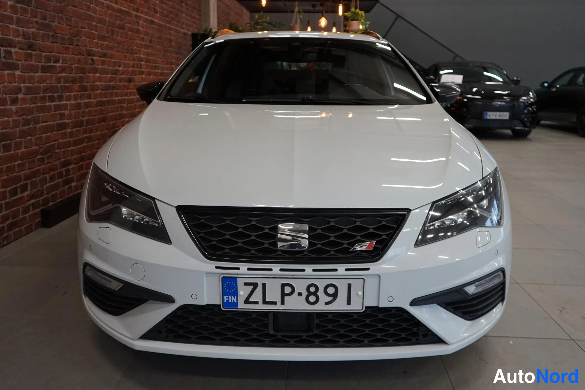 Edestä: Valkoisen Seat Leon ST:n etupää suoraan edestä kuvattuna, ruudukko ja rekisteritunnus näkyvissä.