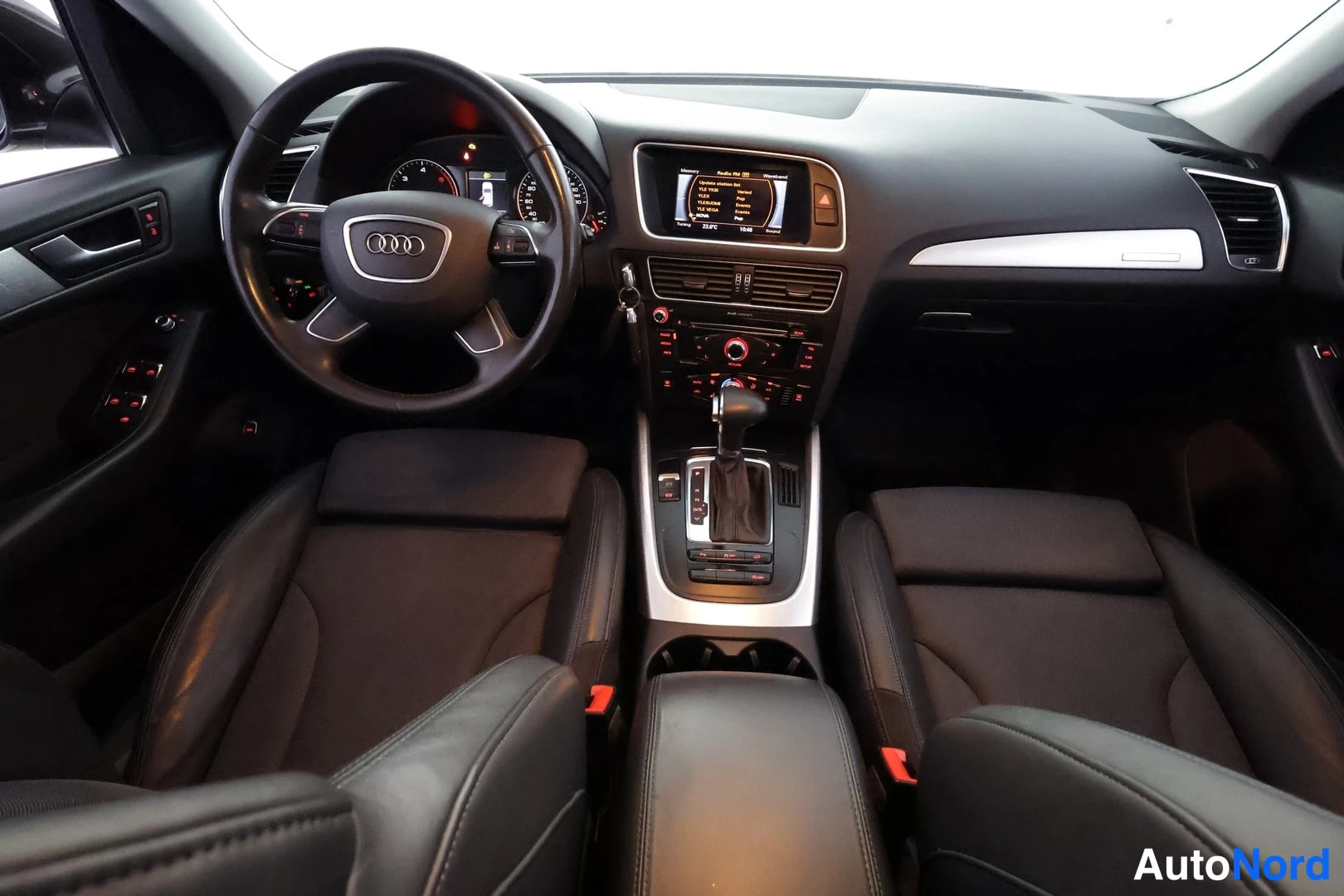 Muu: Auton sisätila kuvattuna takaa: Audi-ohjauspyörä, mittaristo, keskikonsolin näyttö ja vaihdevipu, etupenkit mustaa nahkaa.