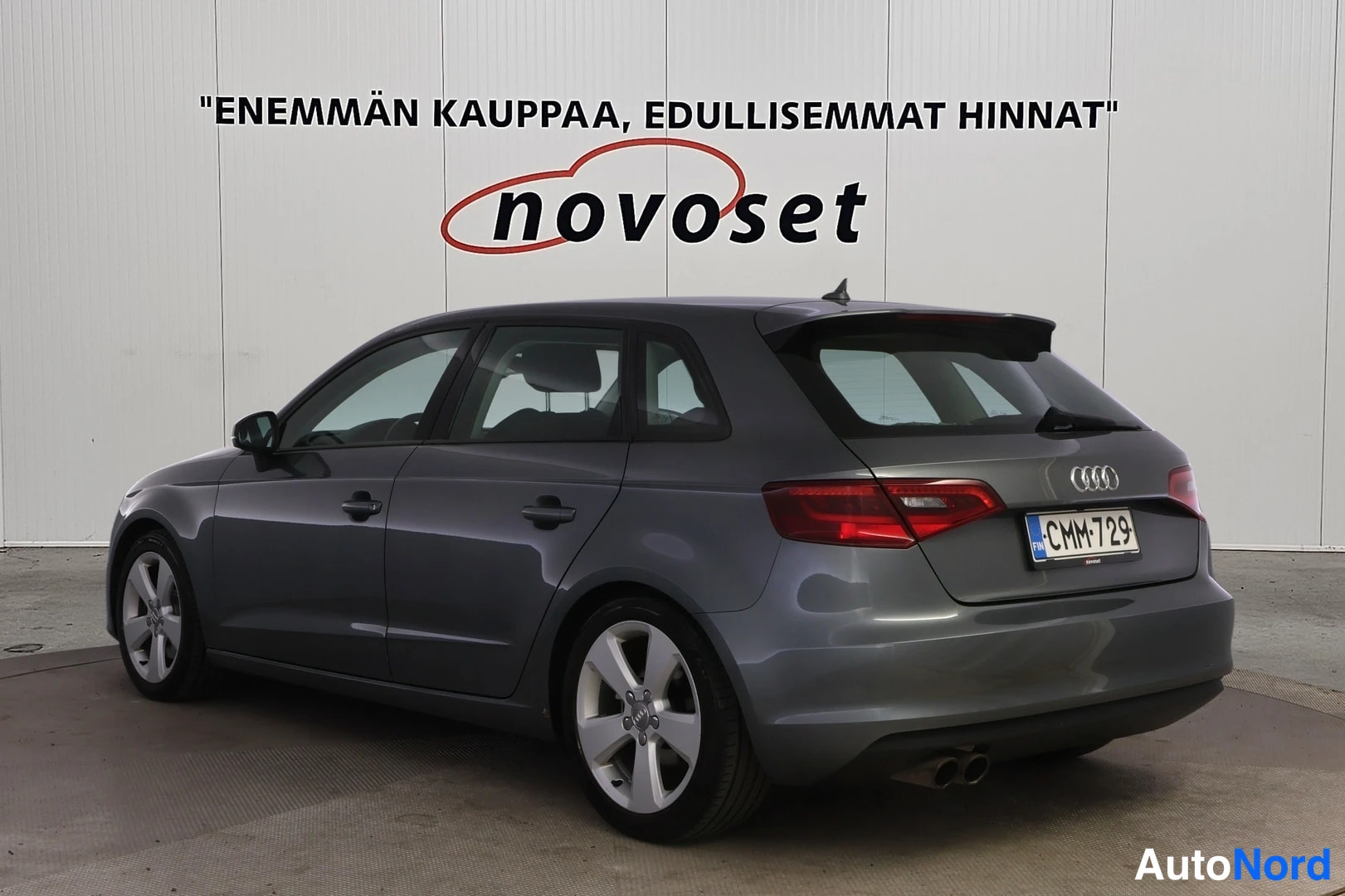 Takaviisto: Harmaa Audi A3 Sportback takaviistöstä vasemmalta kuvattuna autosalon seinustalla.