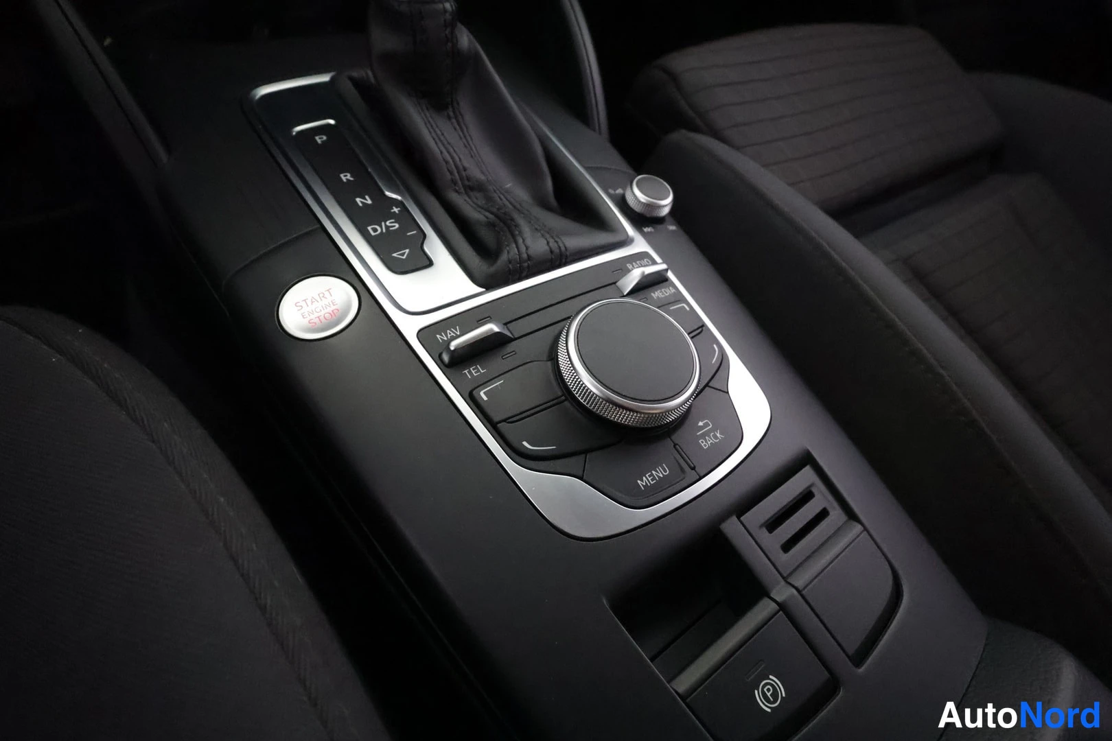 Muu: Sisäkuva keskikonsolista: automaattivaihteen valitsin, START ENGINE STOP -painike, NAV-, TEL-, RADIO-, MEDIA-, MENU- ja BACK-napit sekä pyöreä hallintaohjain.