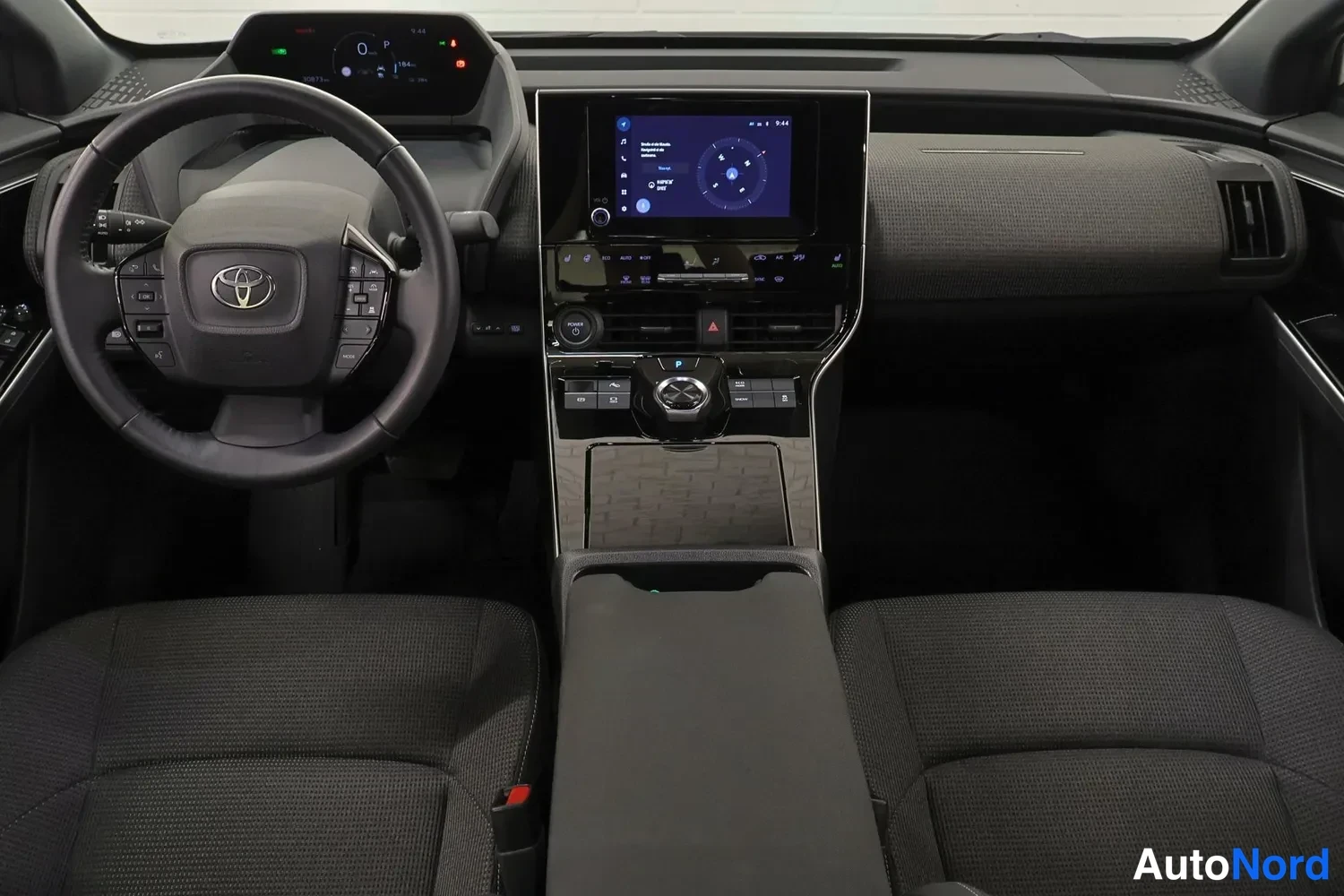 Muu: kojelauta ja ohjaamo ylhäältä: ohjauspyörä Toyota-merkillä, keskellä infotainment-näyttö ja vaihteenvalitsin, tummat kankaaverhoillut etuistuimet