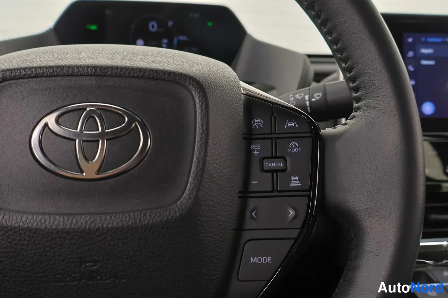 Yksityiskohta: Toyotan ohjauspyörän oikea puoli: ristikkäisavustimen ja kaistavahtimerkkien painikkeet, RES/+/CANCEL/MODE-napit ja kuvakkeita; keskusnäyttö taustalla.