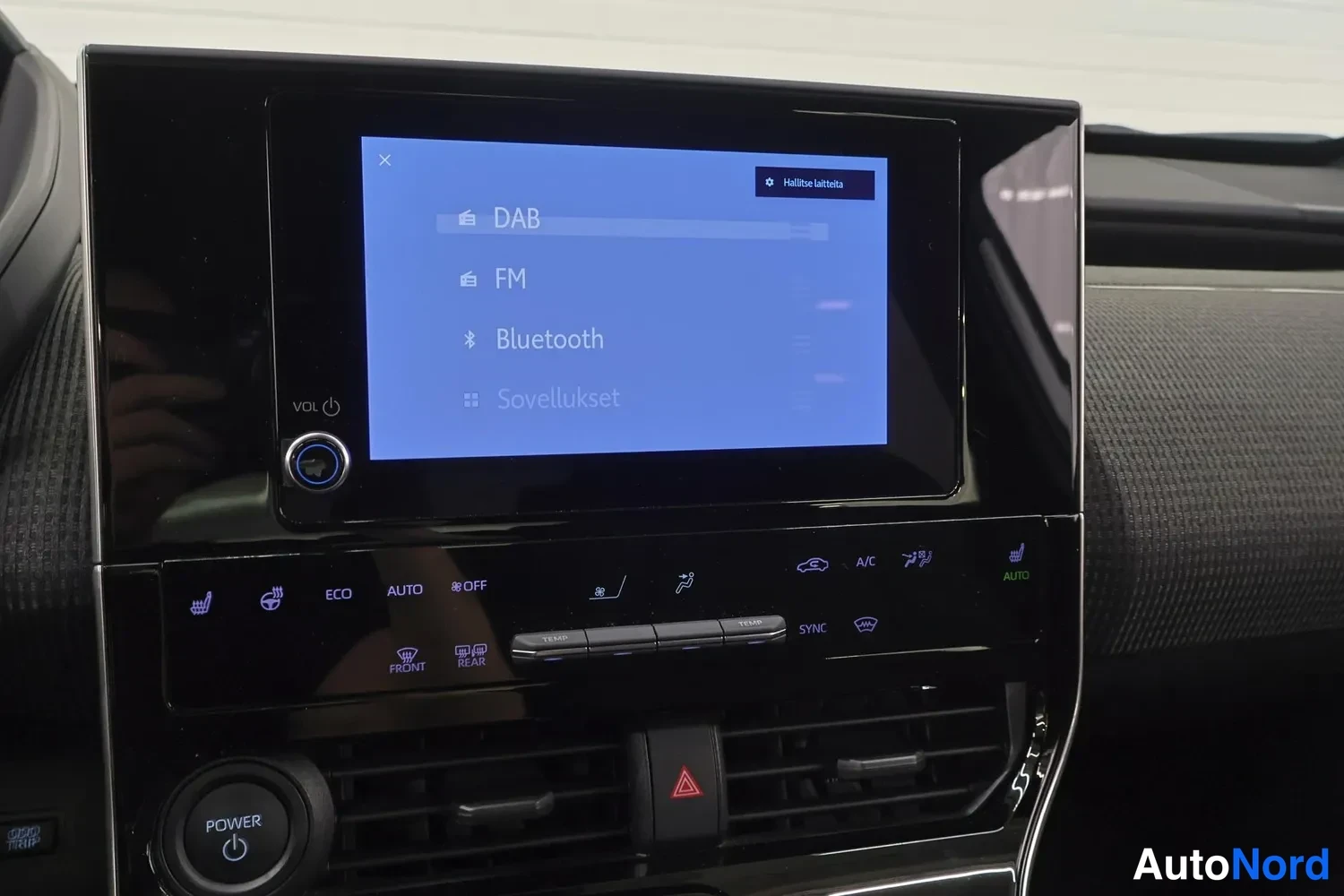 Yksityiskohta: Keskikonsolin näyttö valikossa kohteilla DAB, FM, Bluetooth ja Sovellukset; alla ilmastointipaneeli ja POWER-painike.