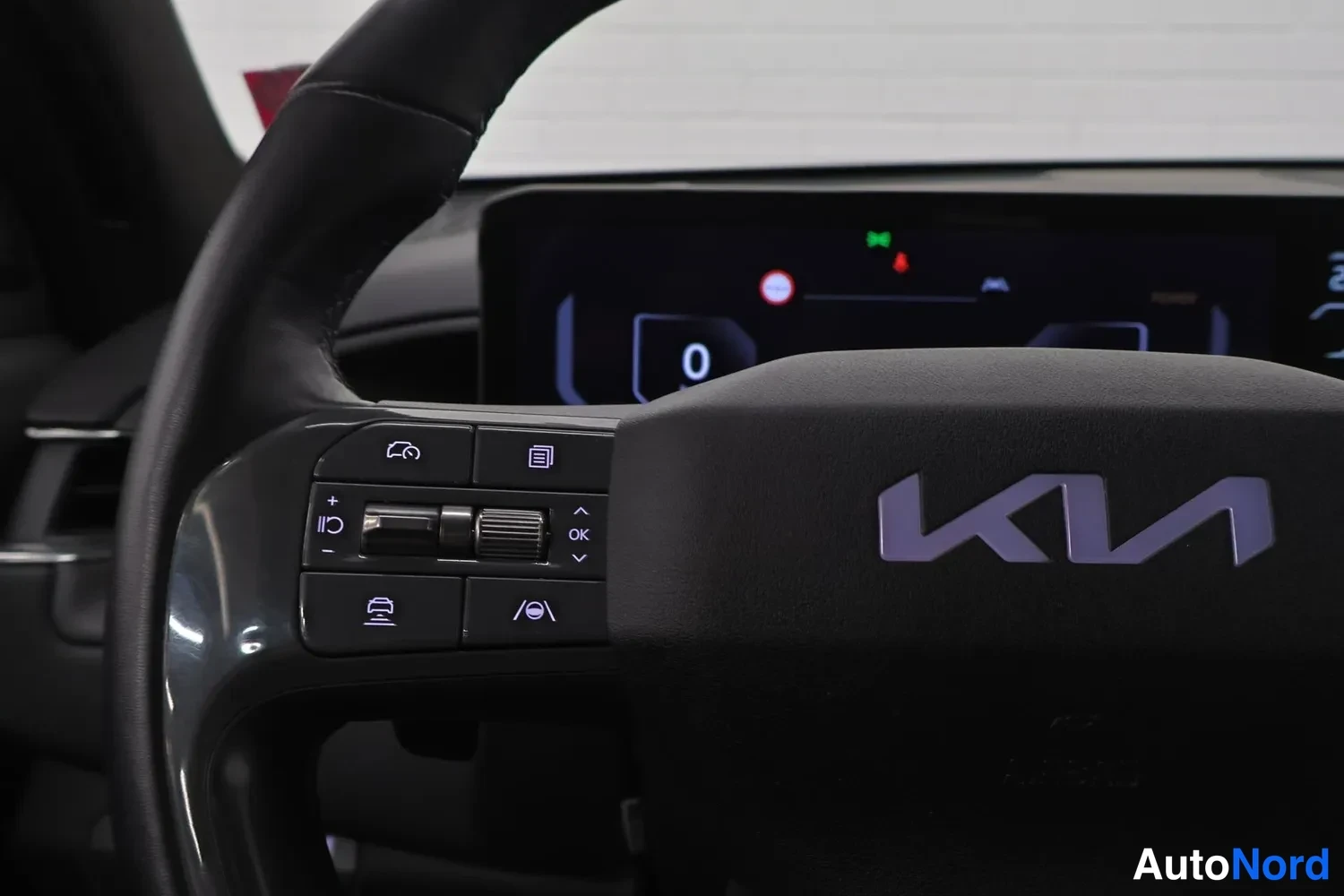 Muu: Ratin vasen puuosi lähikuvassa: Kia-logo, monitoiminapit ja digitaalinen mittaripito näytöllä lukema 0.