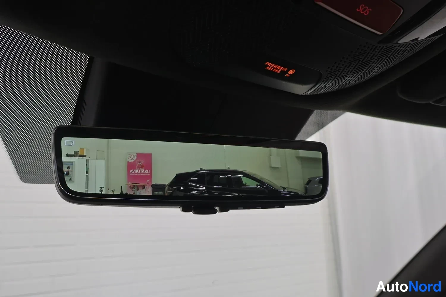 Yksityiskohta: Auton sisäpeili, josta heijastuu tila ja toinen musta auto; kattoosassa SOS-painike ja matkustajan turvatyynyn merkkivalo.