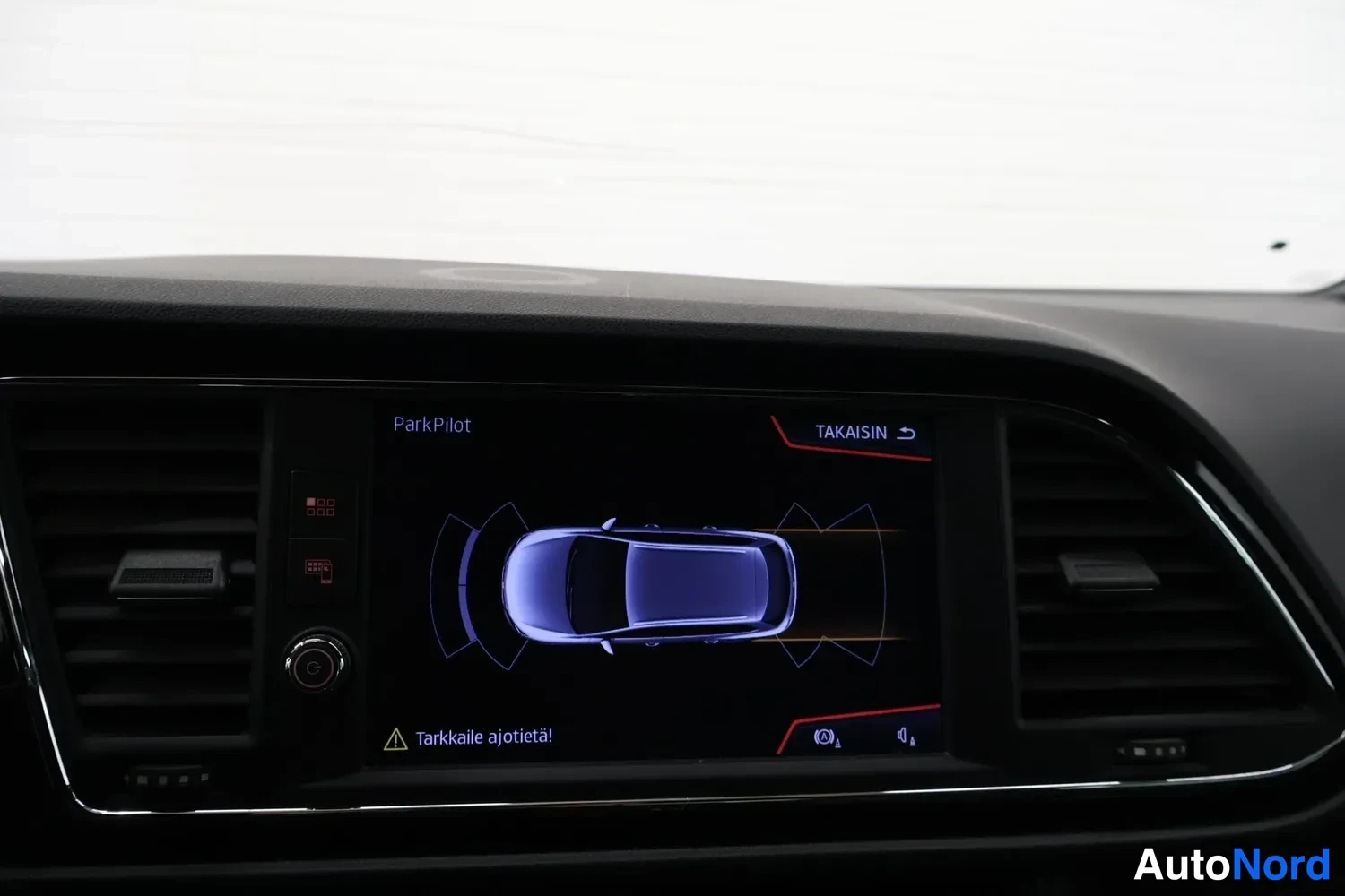 Muu: Keskiössä infotainment-näyttö, jossa ParkPilot-parkkitutkan auton ympärileikkaus ja teksti 'Tarkkaile ajotietä'.