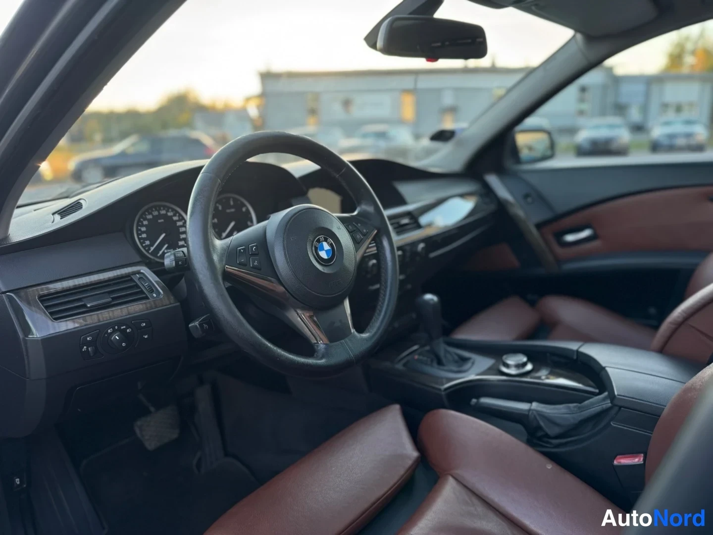 Muu: Autoa kuvattu sisältä kuljettajan puolelta: BMW-ohjauspyörä, mittaristo ja ruskeat nahkaistuimet näkyvät.