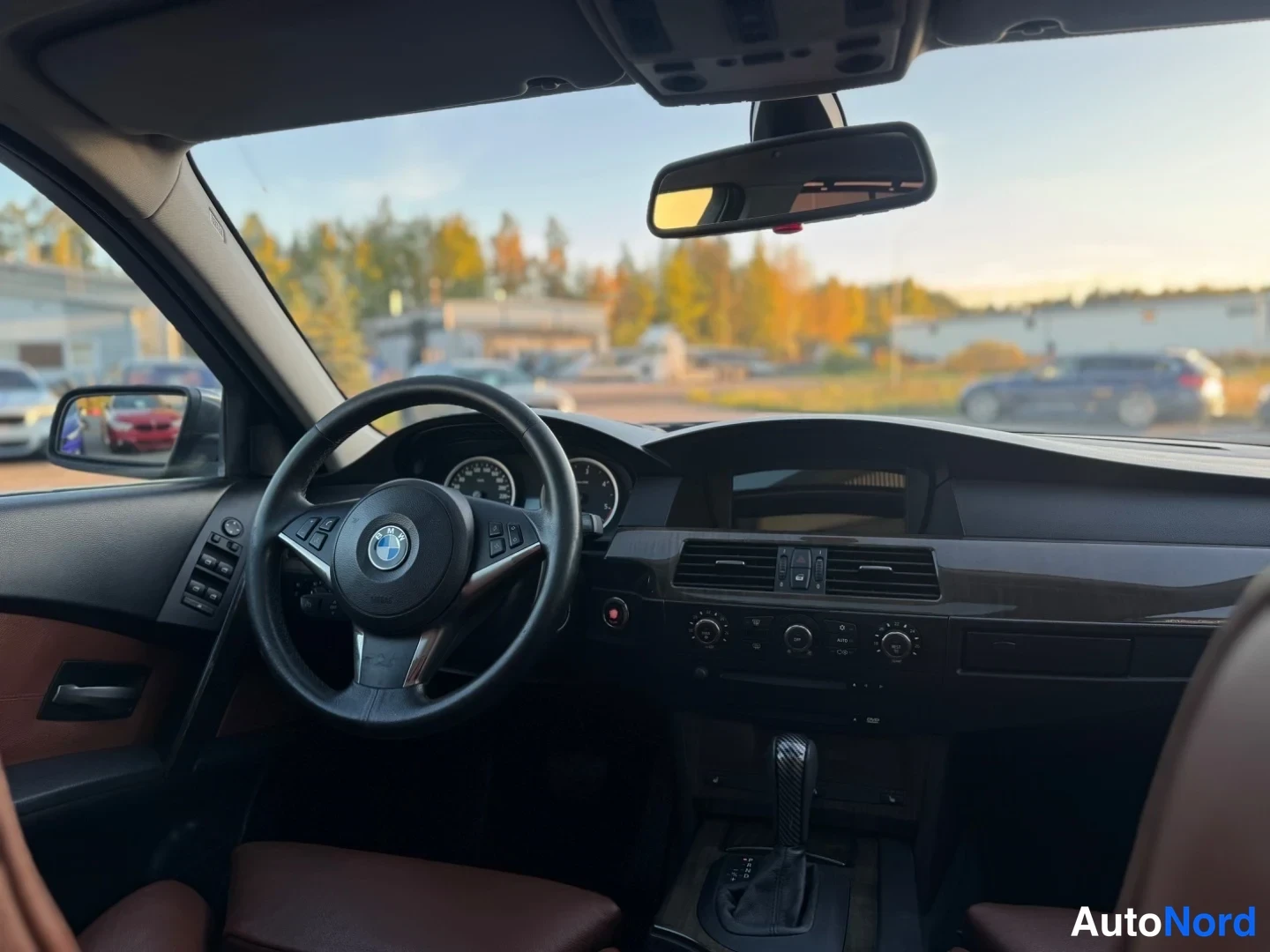 Takaa: Kuljettajan näkökulma sisätiloissa: BMW-ohjauspyörä, mittaristo ja kojelauta näkyvät, ruskeat istuimet.