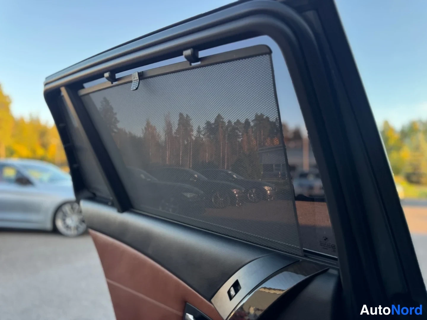 Takaa: Auton takaoven sisäpuolella tukeva musta kudottu aurinkoverho, ympärillä ruskeaa nahkaa.