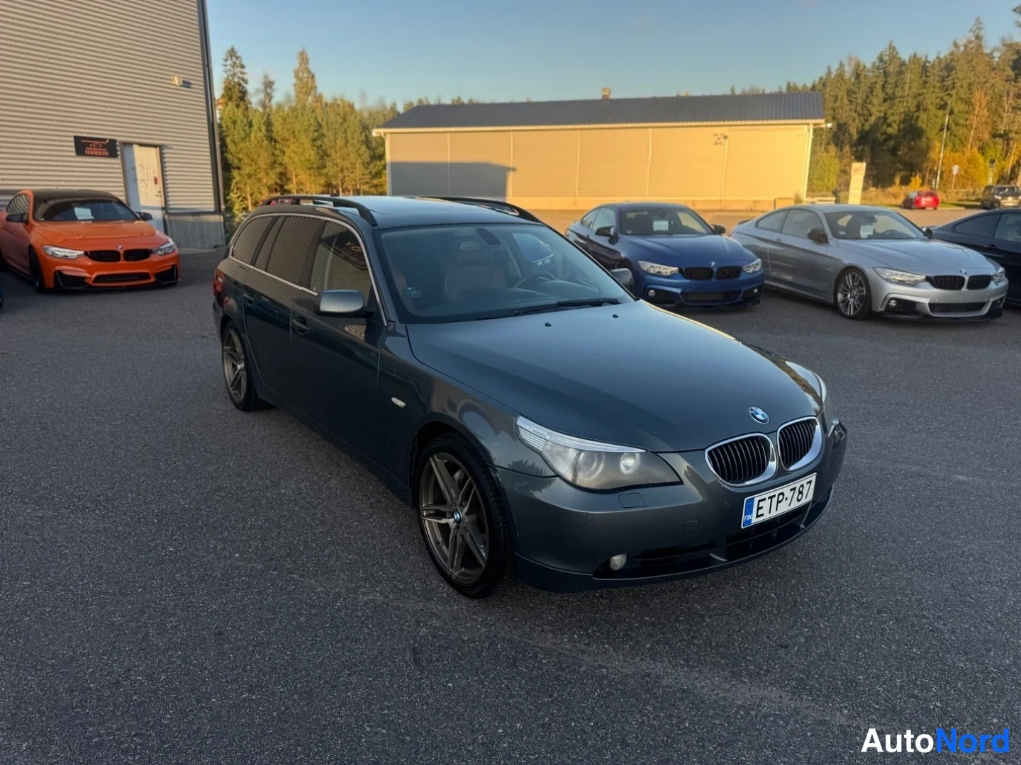 Etuviisto, nokka oikealle: Tummanharmaa BMW 5-sarjan farmari kulmatrista kuvattuna edestä oikealta, rekisteritunnus.